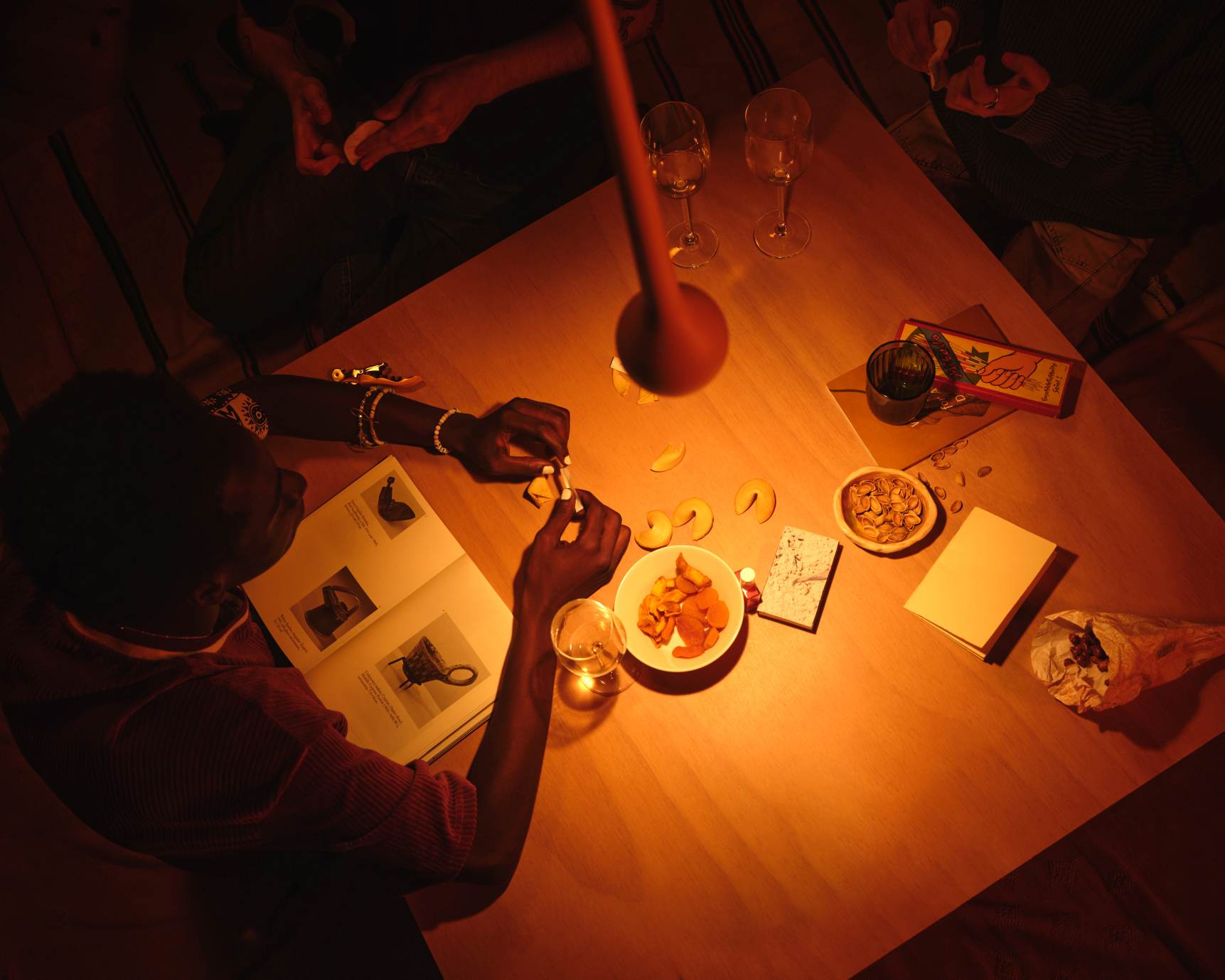 Nahaufnahme: Esstisch beleuchtet durch graue Falling Sun Pendelleuchte, Menschen genießen Snacks und Getränke.