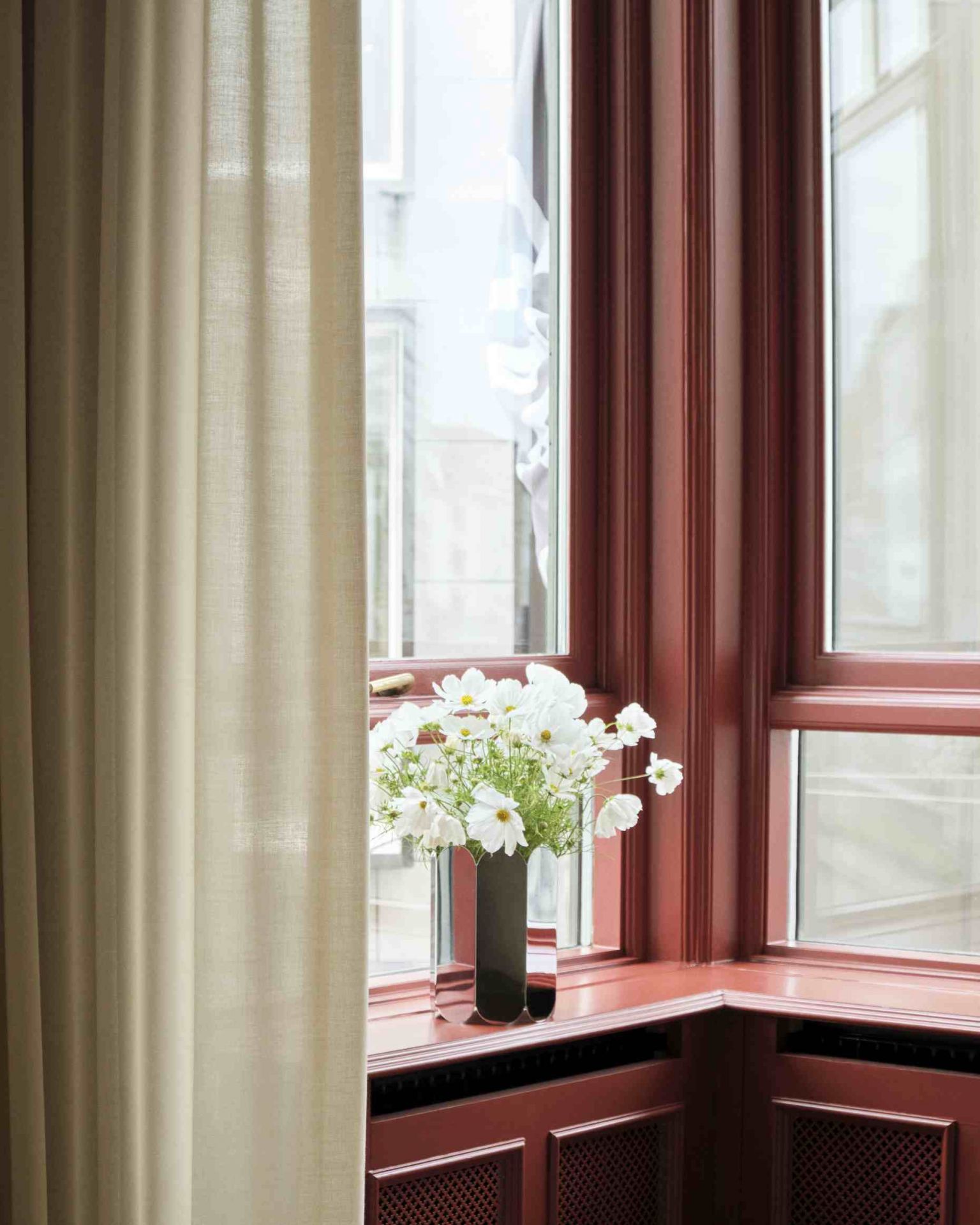 Nahaufnahme der Hay Arcs Vase L Mirror, gefüllt mit weißen Blumen, auf einer Fensterbank.