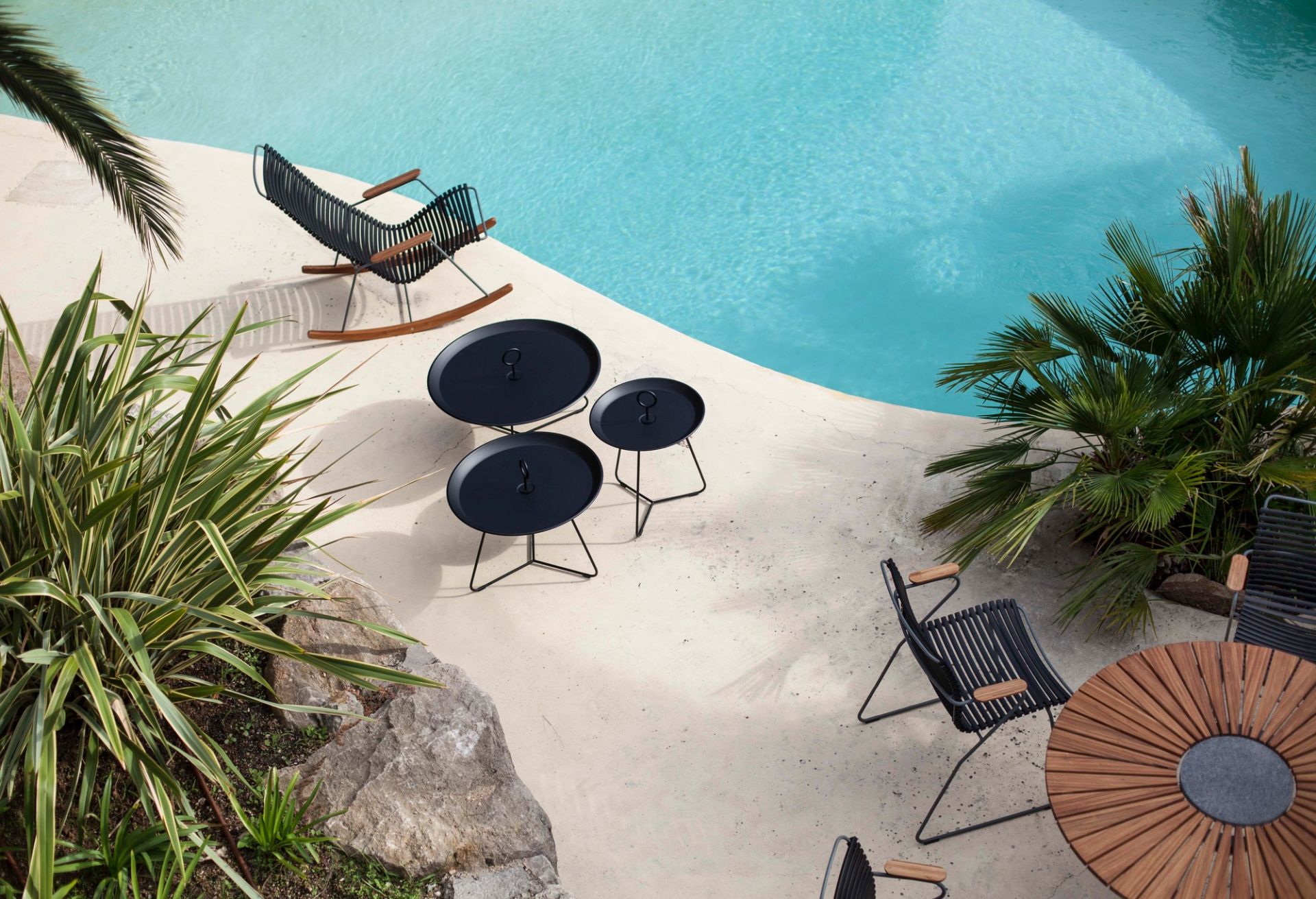 Drei schwarze Eyelet Beistelltische von Houe im Outdoor-Bereich neben einem Pool und Gartenmöbeln.