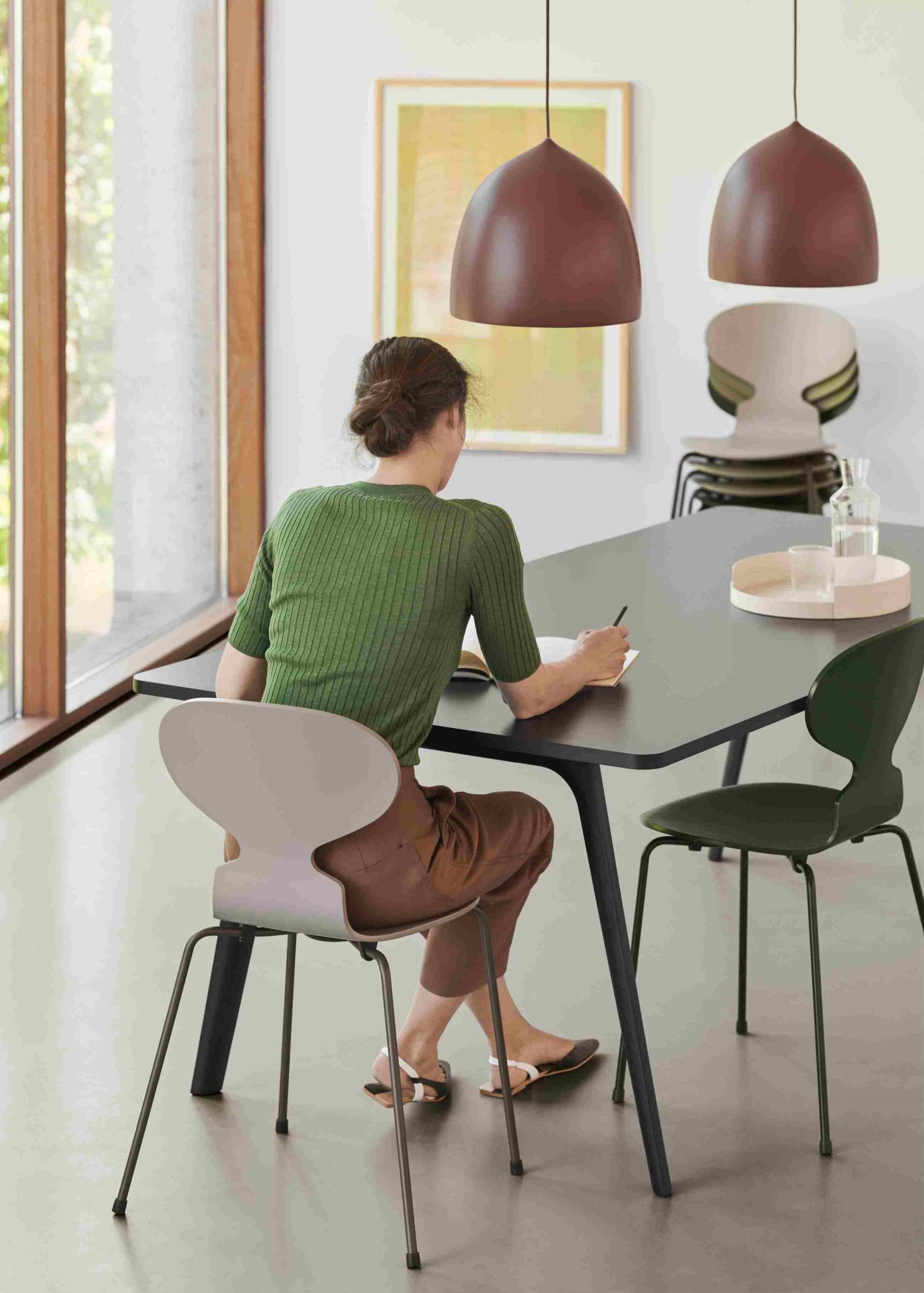 Frau sitzt am Tisch auf einem Fritz Hansen Ameise Stuhl mit vier Beinen in Beige.