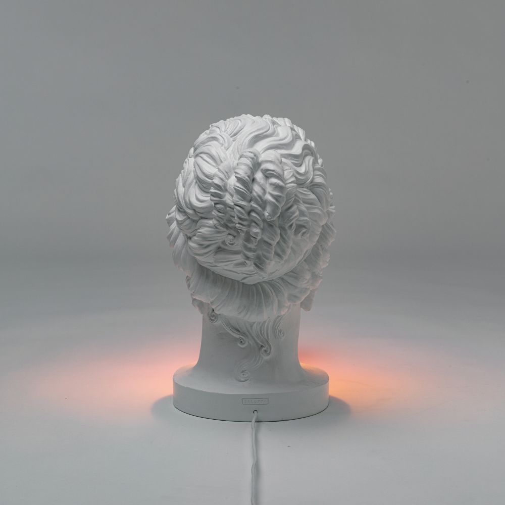 Rückansicht der weißen Grace Lamp Tischleuchte von Seletti, die ein warmes Licht ausstrahlt.