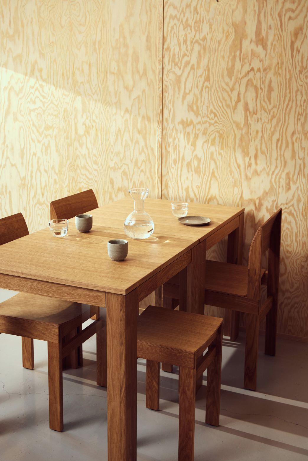 Sonder Stuhl Form & Refine: Esstisch mit Stühlen aus hellem Holz, gedeckt mit Karaffe und Gläsern.