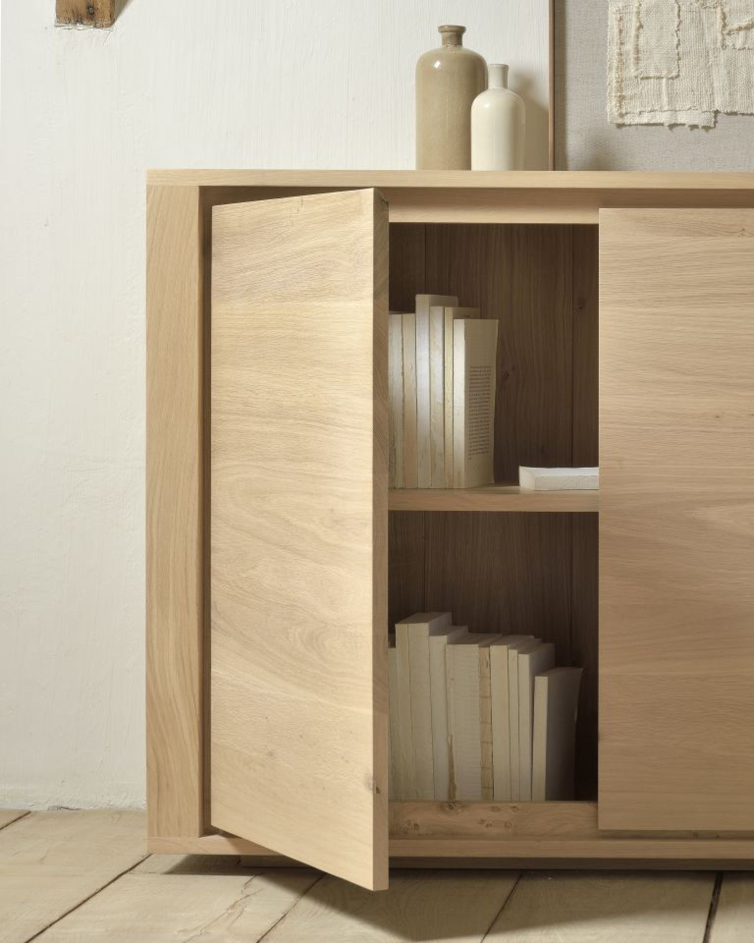 Detailaufnahme des Ethnicraft Shadow Sideboards aus Eiche mit geöffneter Tür und Büchern.