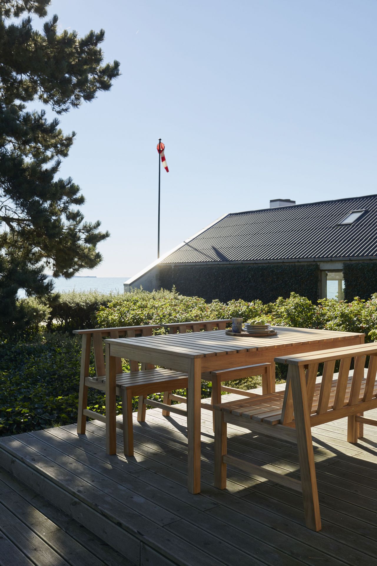 Cadence Bank Teak Gartengarnitur von Fritz Hansen auf Holzterrasse mit Blick auf Garten und Meer.