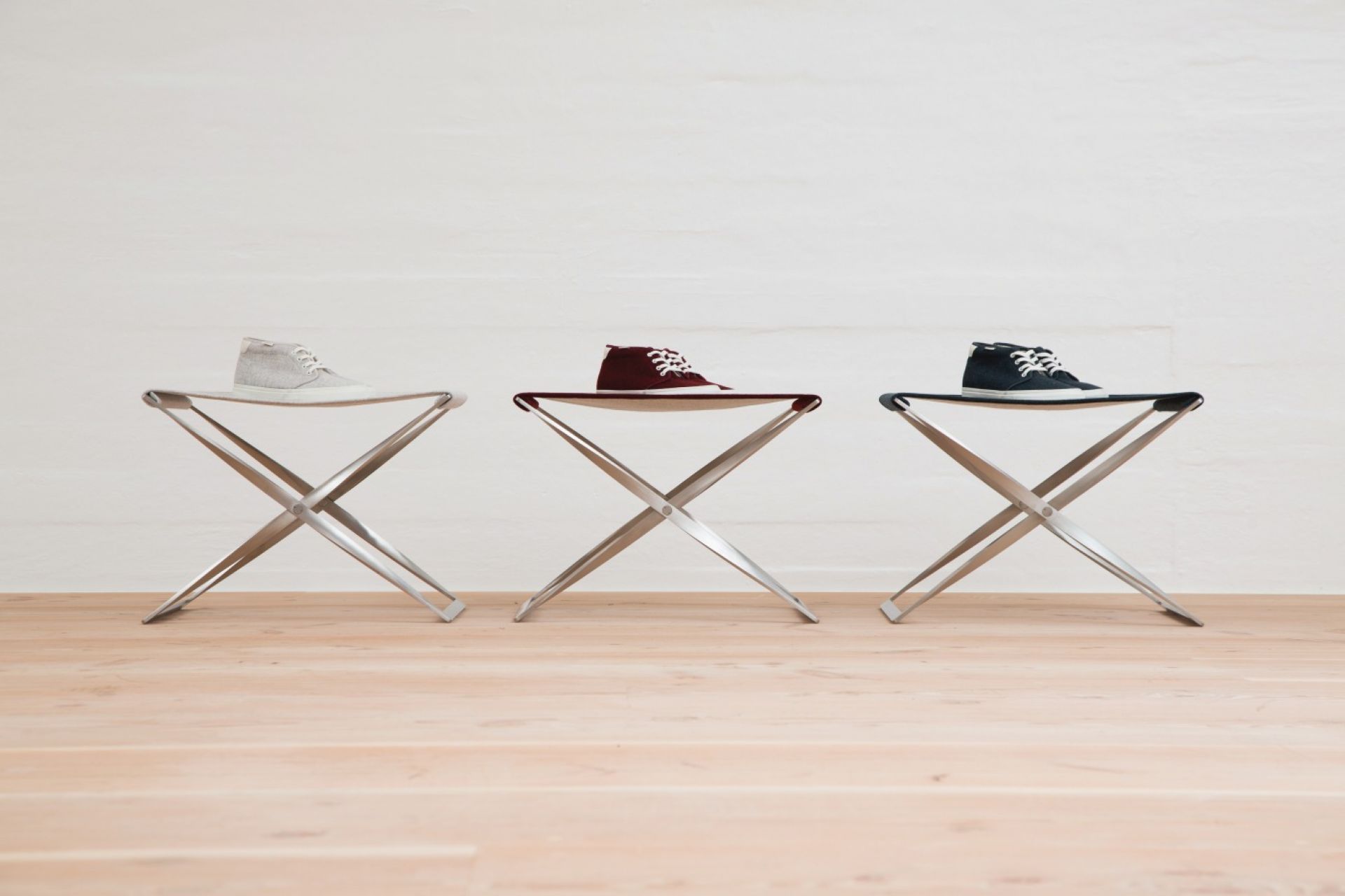 Drei PK91 Falthocker von Fritz Hansen in Grau, Rot und Blau mit Schuhen darauf.