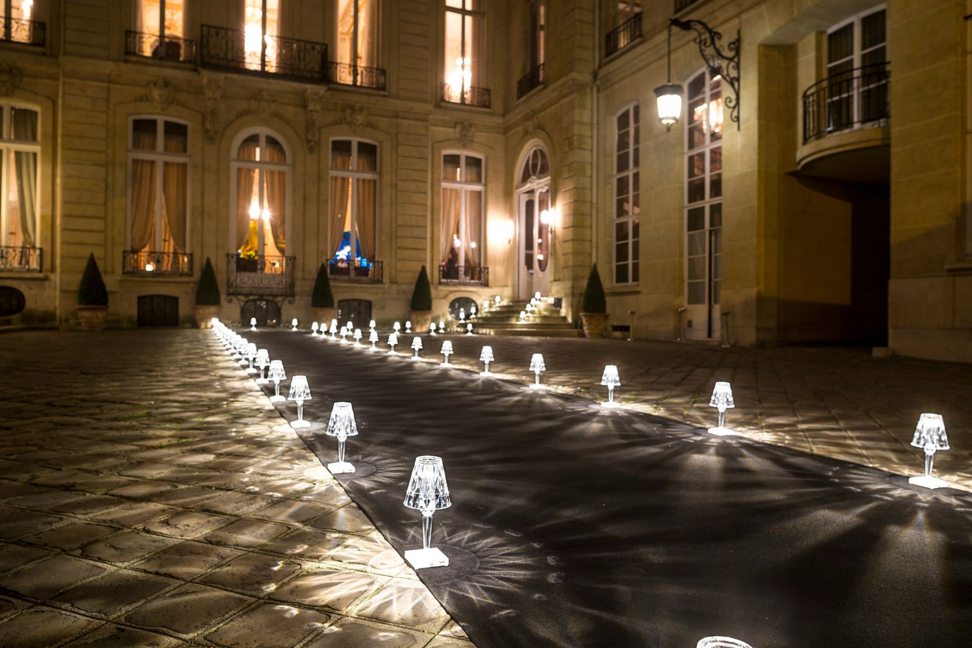 Reihe von Kartell Battery Tischleuchten in Rauch vor einem Gebäude bei Nacht.