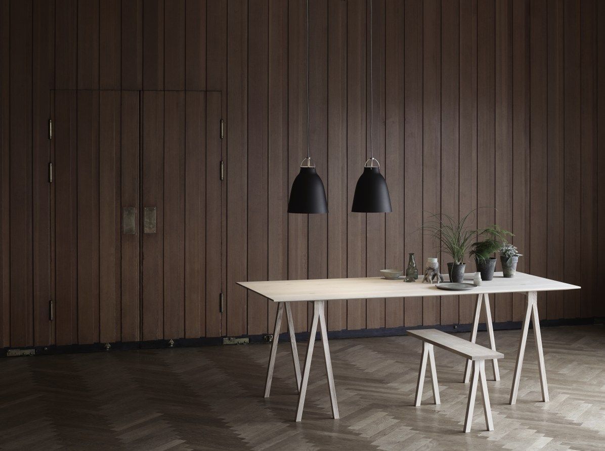 Zwei schwarze Caravaggio Pendelleuchten von Fritz Hansen über einem Esstisch mit Holzbank und Dekoration.