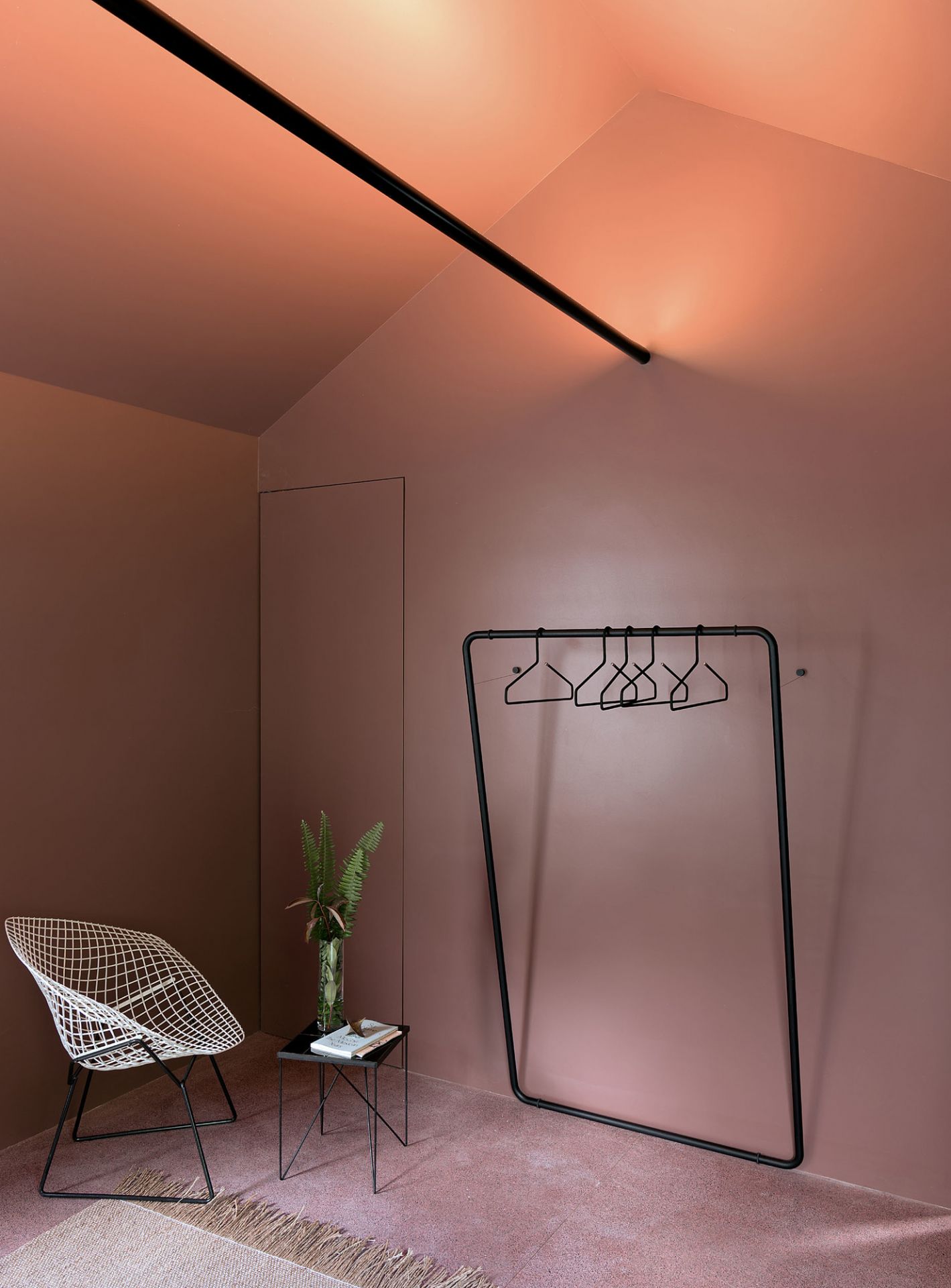 Schönbuch Curve Wandgarderobe in minimalistischem Raumdesign mit Stuhl, Beistelltisch und Kleiderbügeln vor rosa Wand.