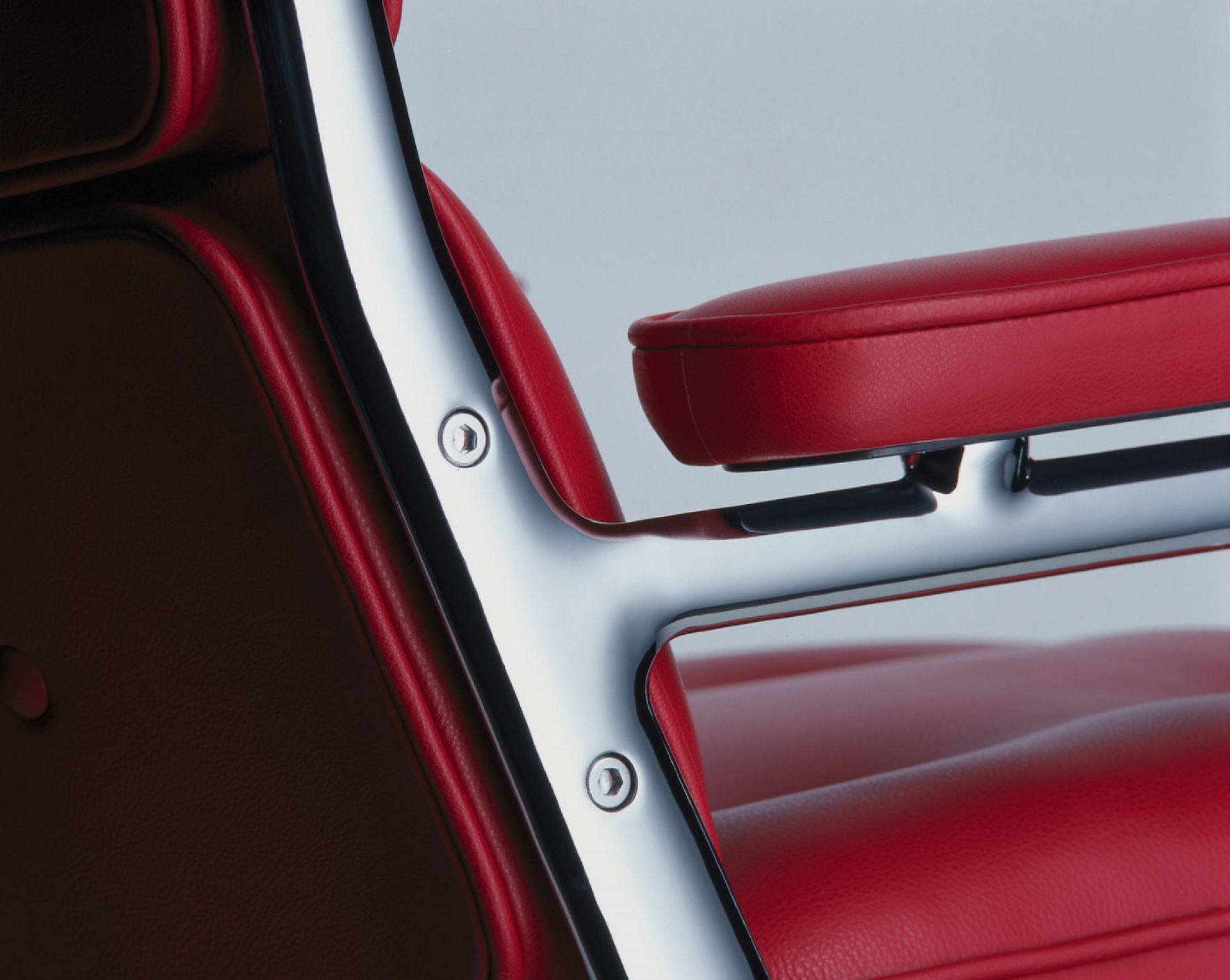 Detailaufnahme des roten Vitra Lobby Chair ES 104 Stuhls mit verchromtem Gestell und Armlehne.