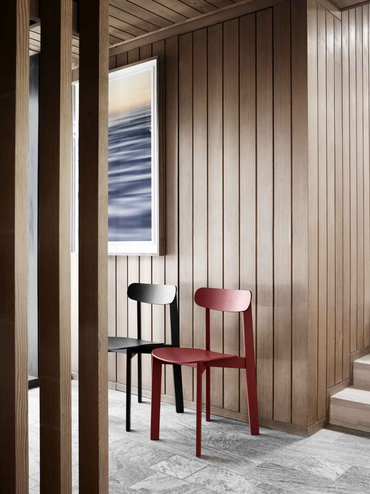 Zwei moderne Holzstühle: Ein schwarzer und ein roter Stuhl vor einer Holzwand.