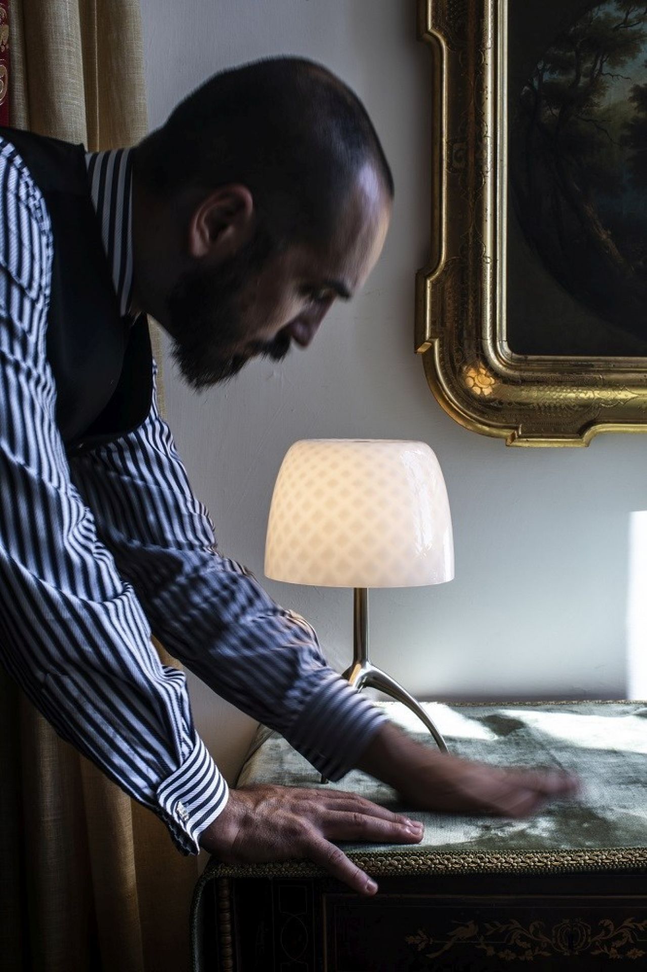 Nahaufnahme der Lumiere Tischleuchte von Foscarini, mit Mann im gestreiften Hemd im Hintergrund.
