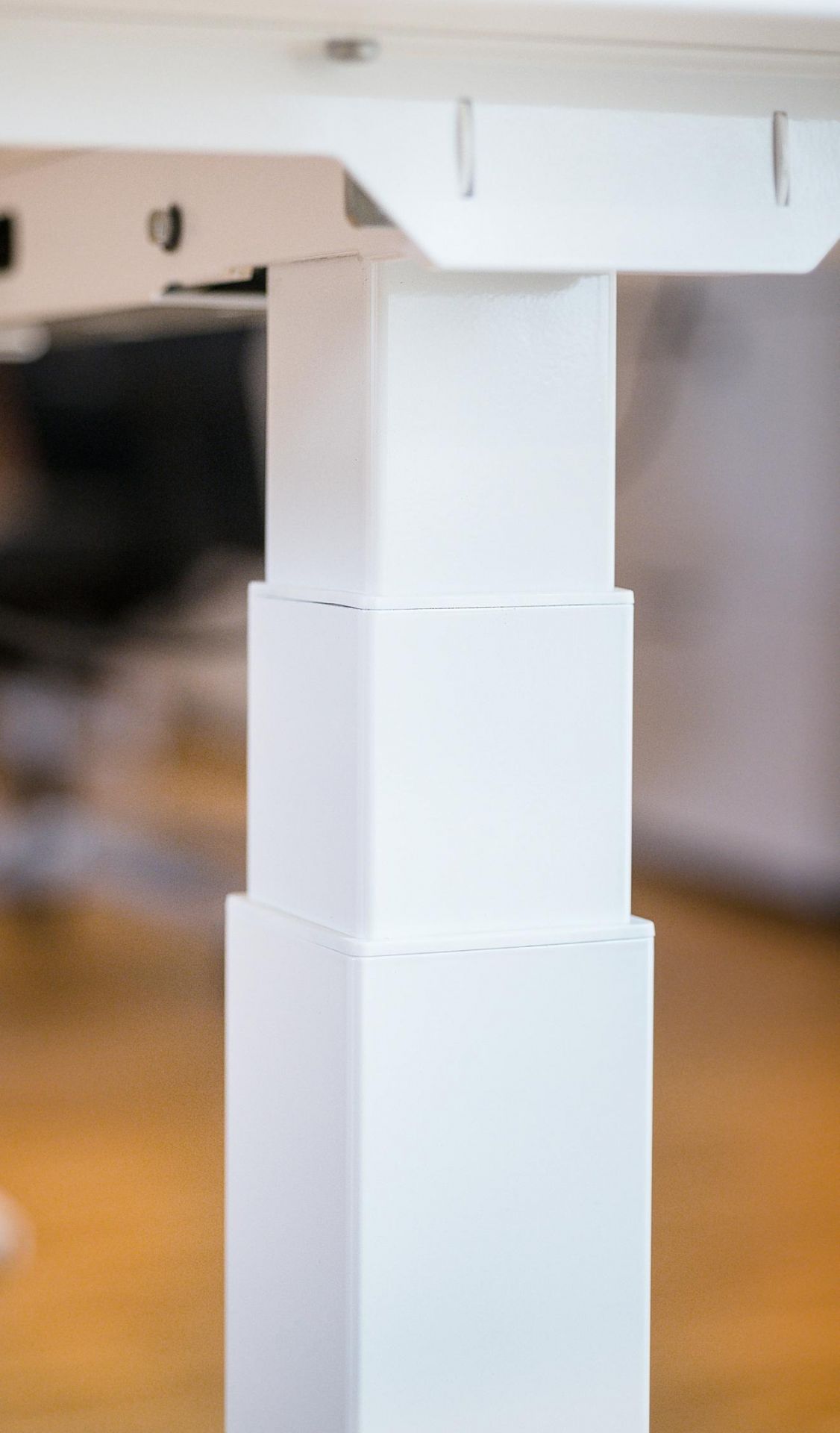 Detailaufnahme des weißen, höhenverstellbaren Hiplift Sitz-Stehtisch-Gestells für ergonomisches Arbeiten im Büro.