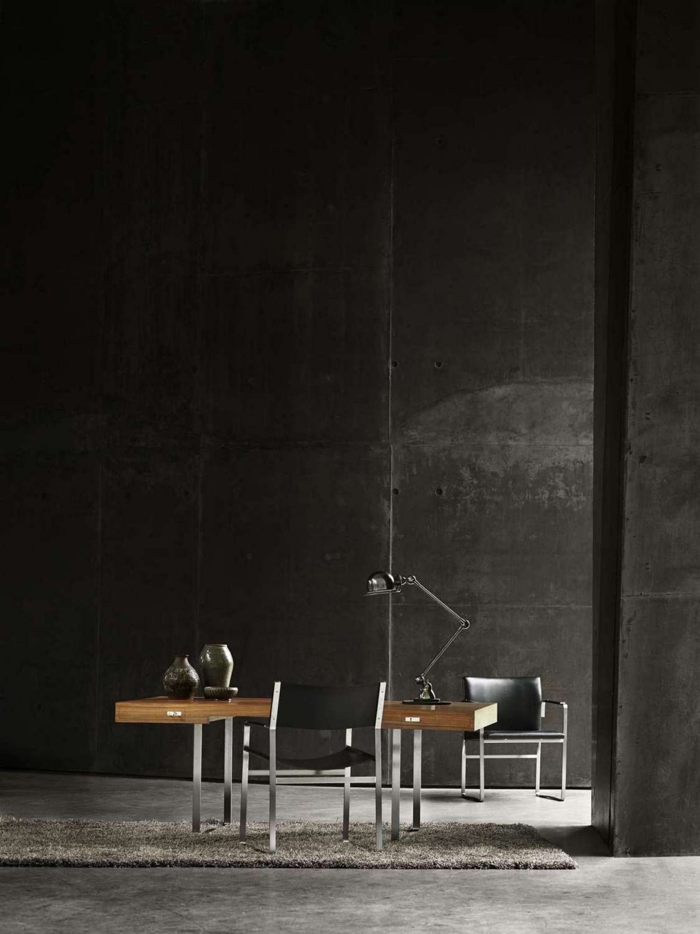 CH110 Tisch von Carl Hansen & Søn mit Stühlen und Lampe vor dunkler Betonwand.