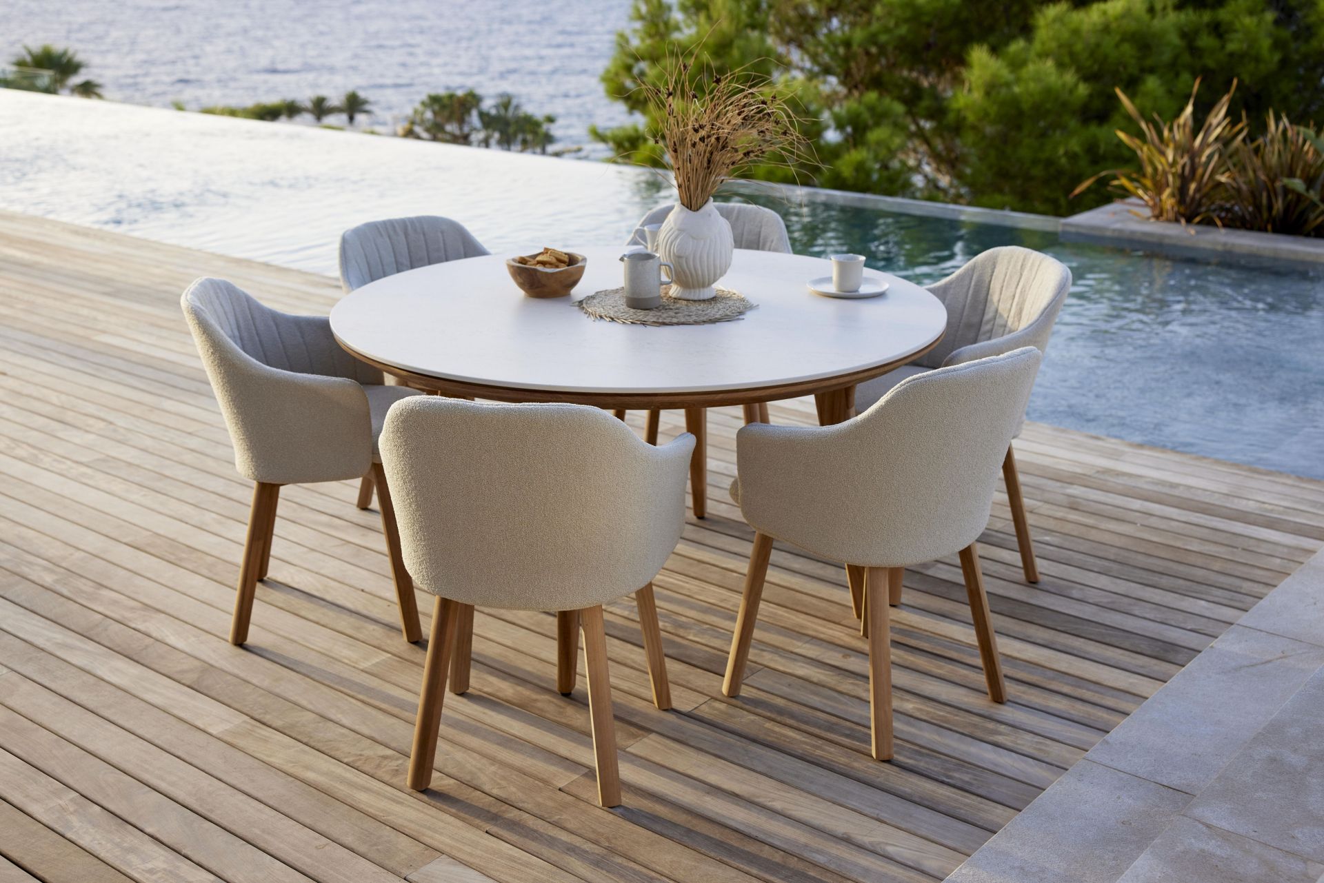 Choice Outdoor Stühle mit Teakgestell um einen runden Gartentisch auf einer Holzterrasse.