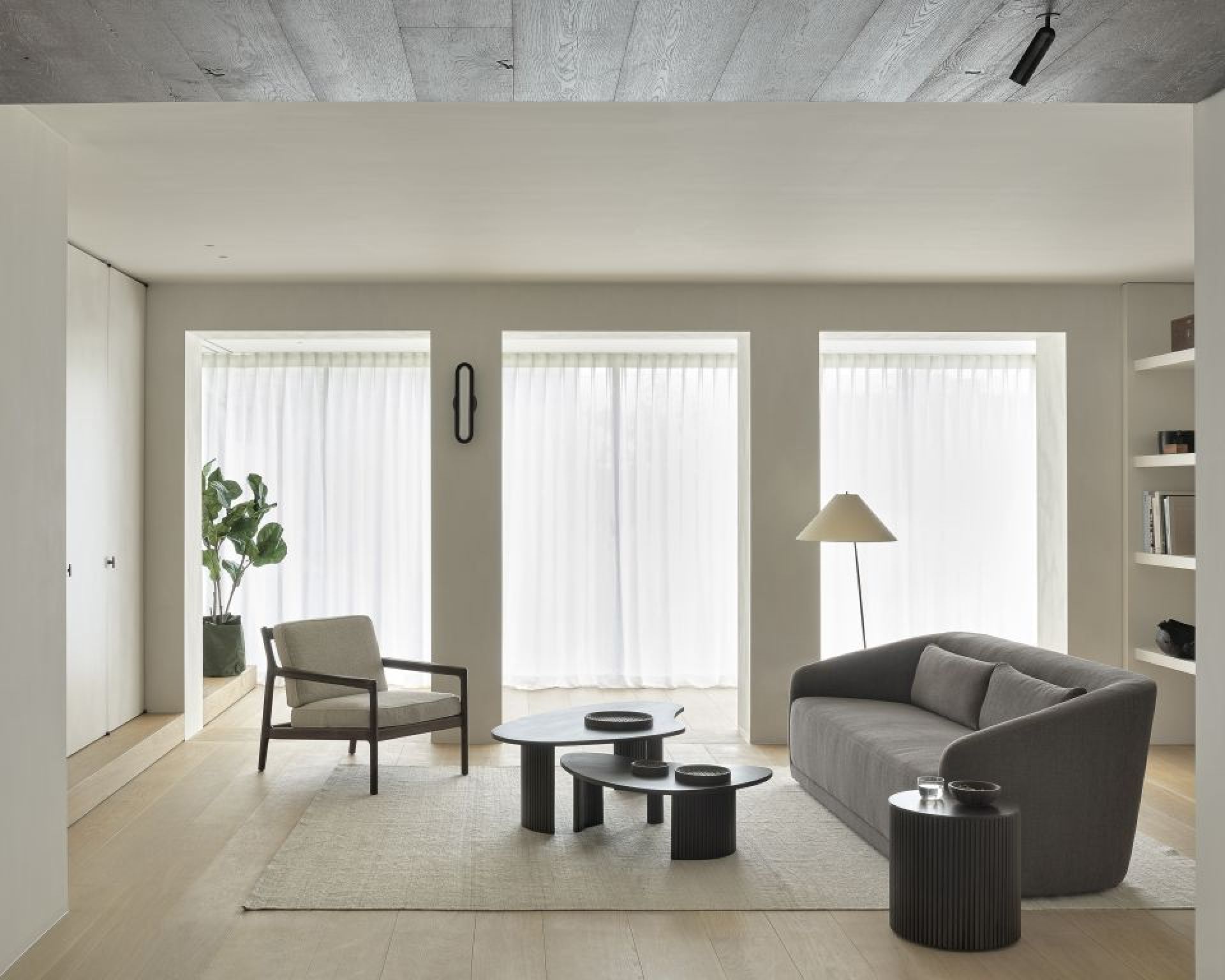 Wohnzimmer-Szene mit Ethnicraft Roller Max Beistelltisch in Dunkelbraun neben grauem Sofa und Couchtischen.