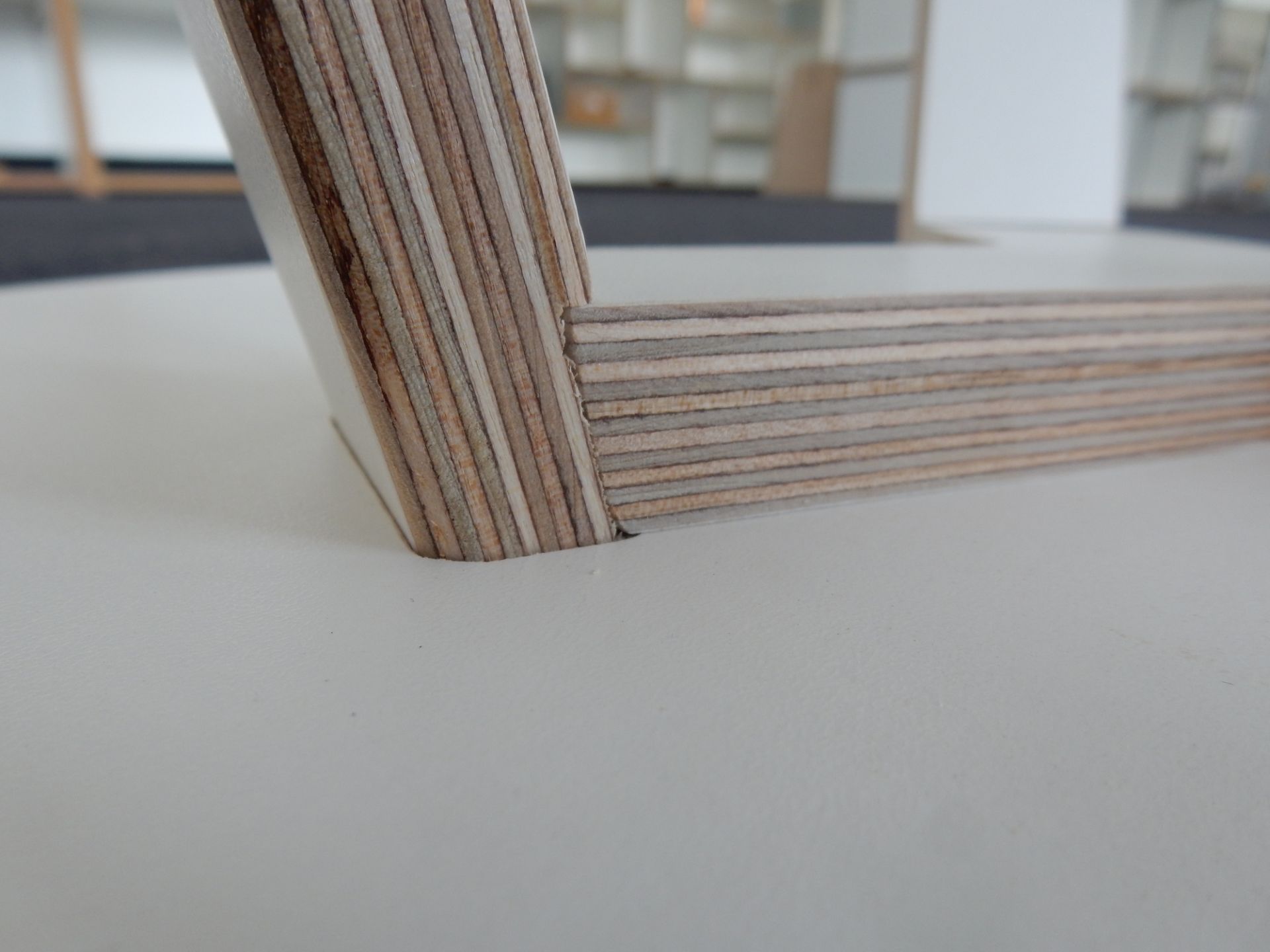 Detailaufnahme vom Tojo Rund Tisch 500: Tischbein aus Schichtholz trifft auf die weiße Tischplatte.