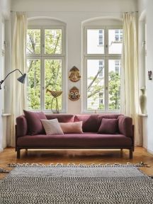 Burgunderrotes Sofa mit mehreren Vitra Kissen in verschiedenen Farben im hellen Wohnzimmer.