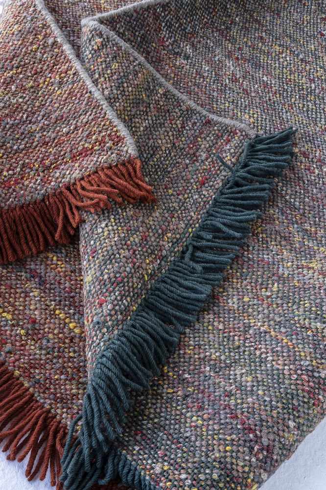 Detailaufnahme des Re-Rug Collection Teppichs von Nanimarquina mit bunten Fasern und dekorativen Fransen in Braun und Grün.