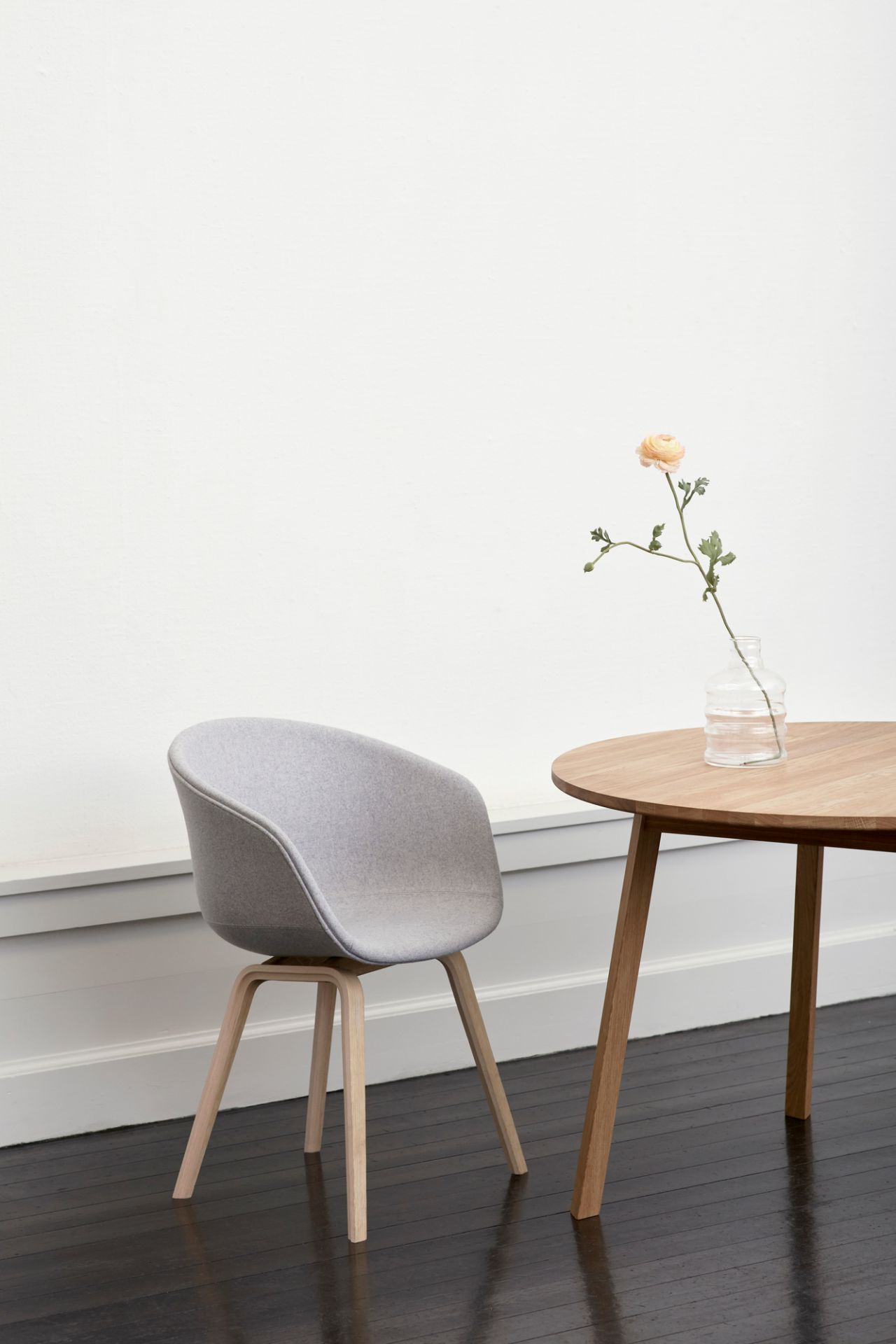 About A Chair AAC23 Stuhl von Hay mit grauem Bezug und Holztisch mit Blume.