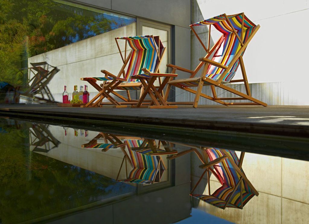 Zwei gestreifte Weishäupl Cabin Strandstühle aus Holz stehen im Freien am Pool.