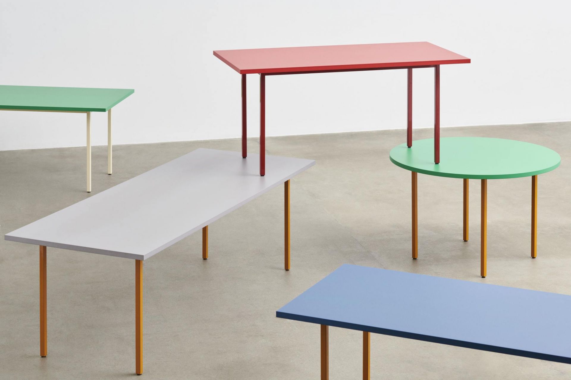Mehrere farbenfrohe Two Colour Table Tische von Hay in verschiedenen Formen und Größen auf beigem Untergrund.
