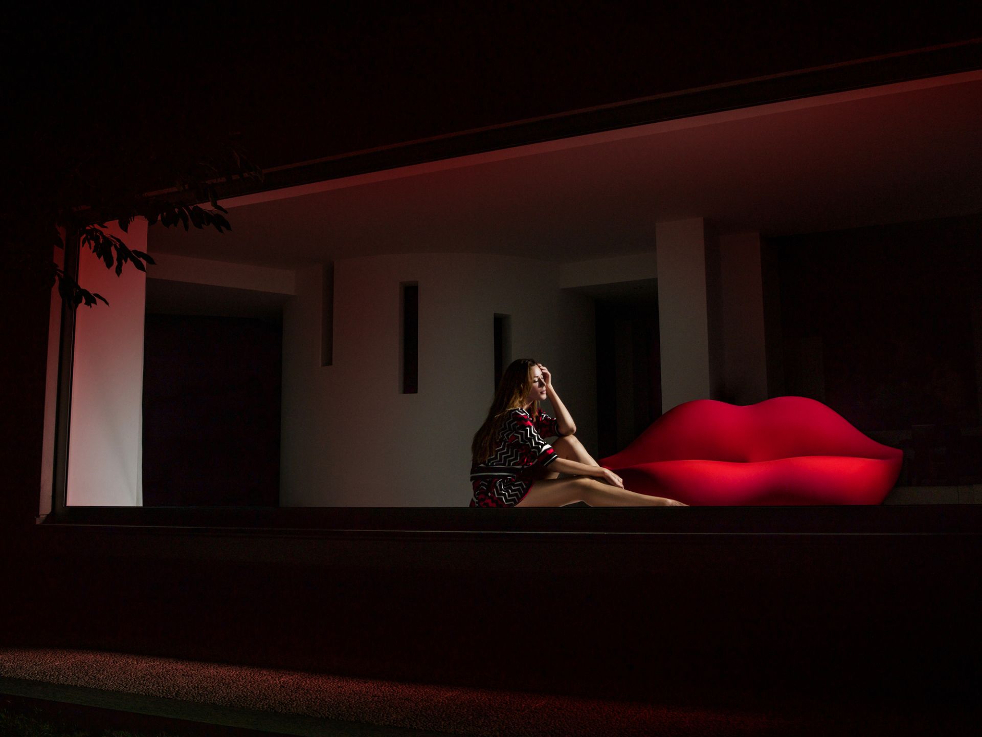 Frau sitzt auf rotem Bocca Sofa von Gufram, Lippensofa, Designmöbel für Wohnzimmer und Lounge.