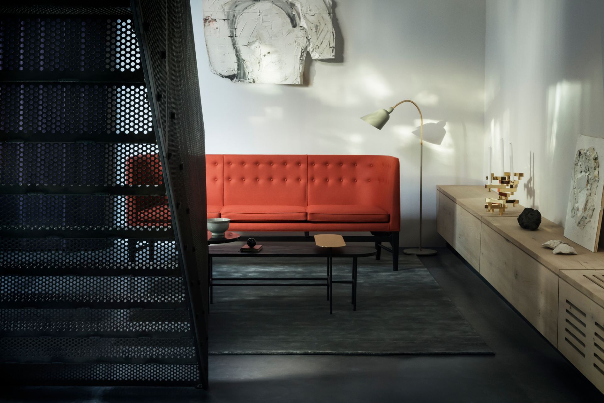 AndTradition Mayor Sofa, roter 3-Sitzer mit Knopfleiste in modernem Wohnzimmer mit Treppe und Kunst.