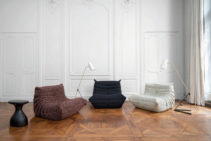 Drei Togo Sessel von ligne roset in verschiedenen Farben auf einem Parkettboden vor einer weißen Wand.