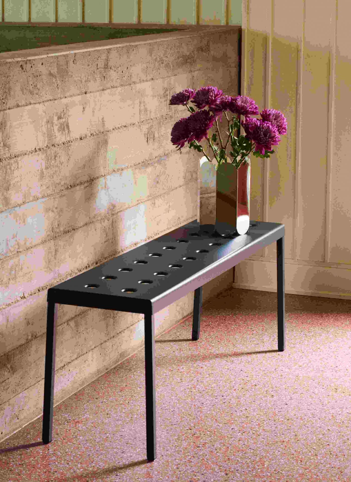 Hay Arcs Vase L Mirror: Spiegeleffekt Vase mit lila Blumen auf einem schwarzen Tisch.