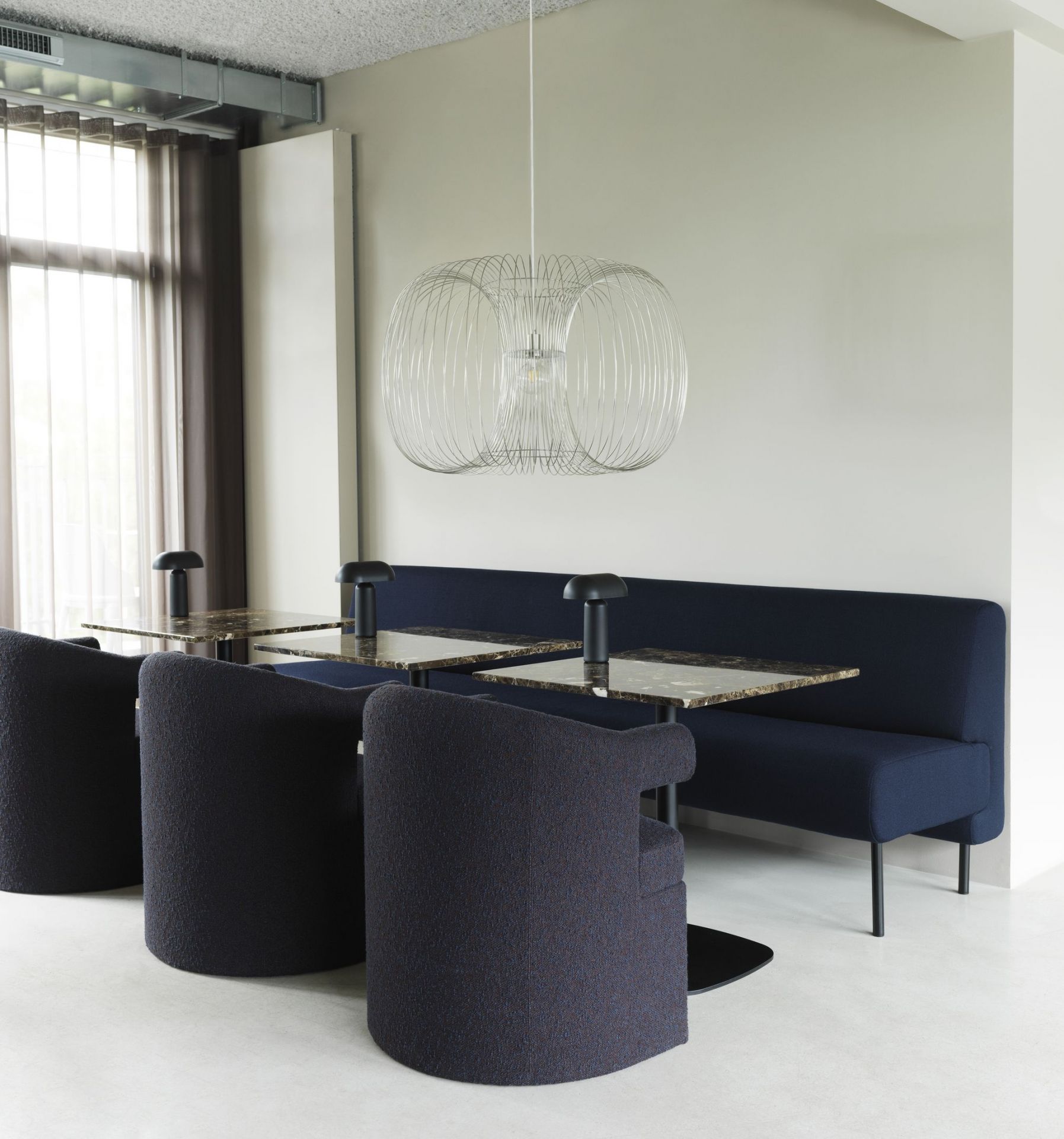 Innenaufnahme mit Burra Chair Stühlen von Normann Copenhagen an Tischen mit dunkelblauer Sitzbank.