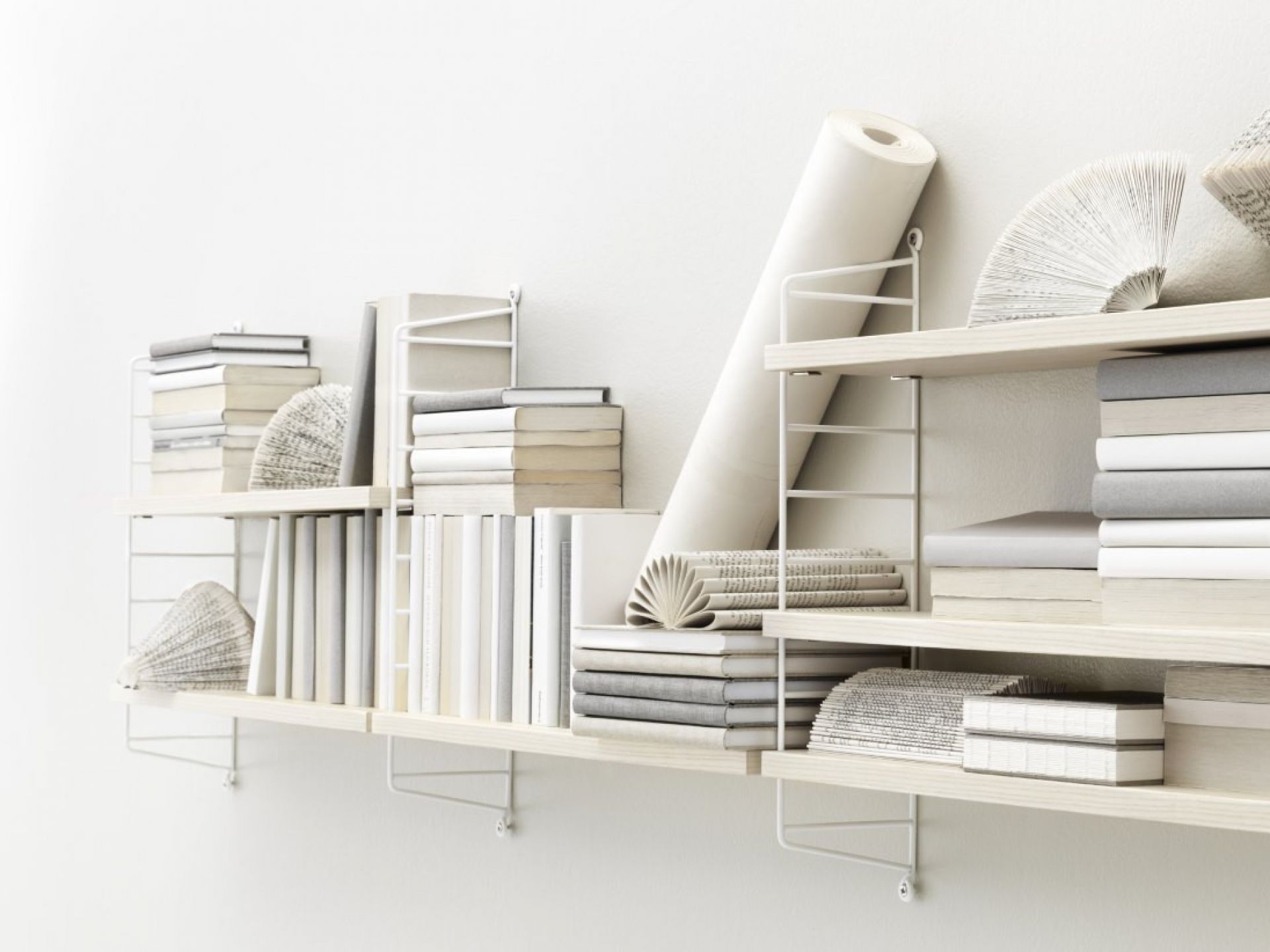 Weißes String Regal mit Büchern und Dekoration an einer weißen Wand.