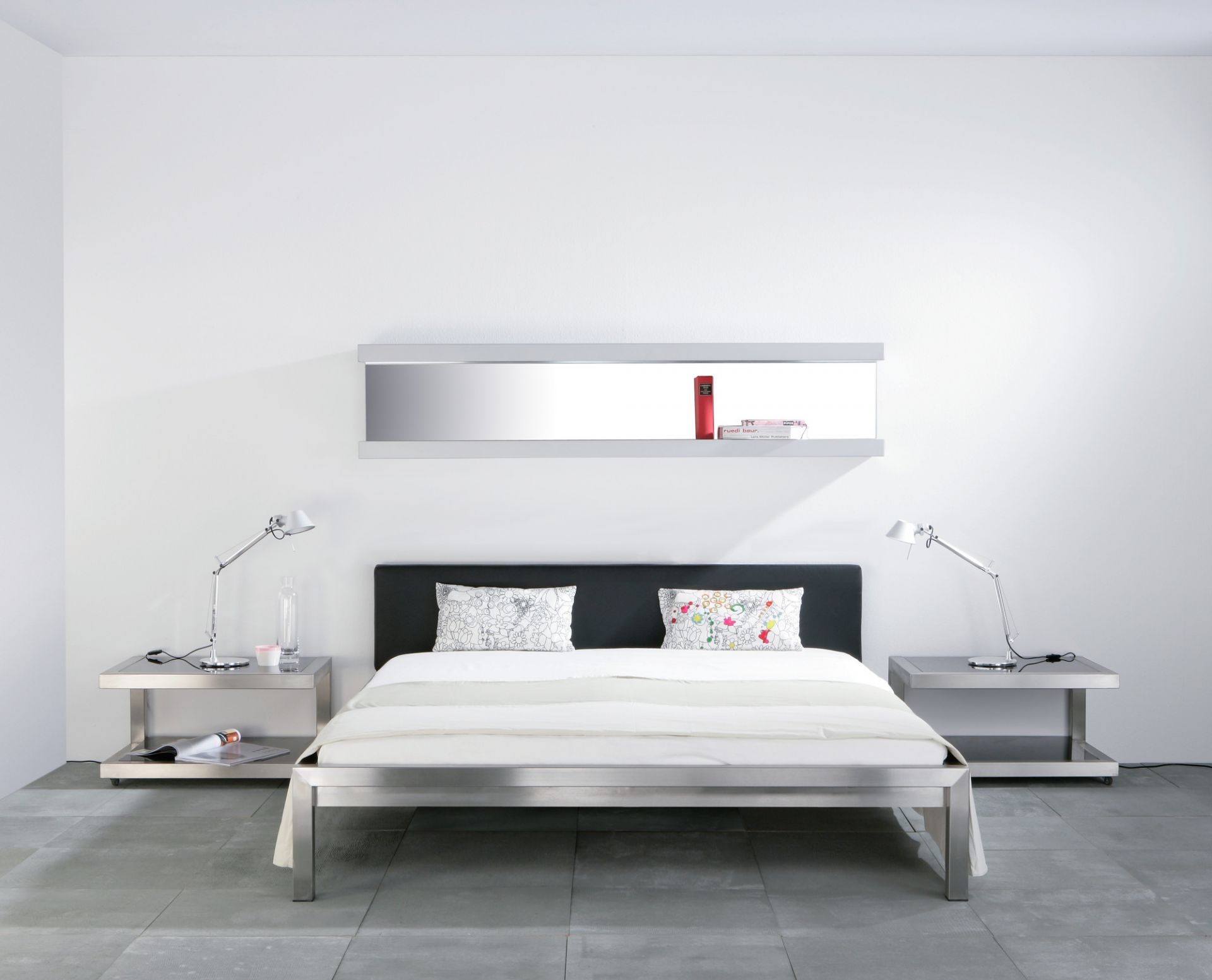 Hans Hansen Pure Bett: Edelstahlbett 160x200 mit schwarzem Polsterkopfteil und passenden Nachttischen.