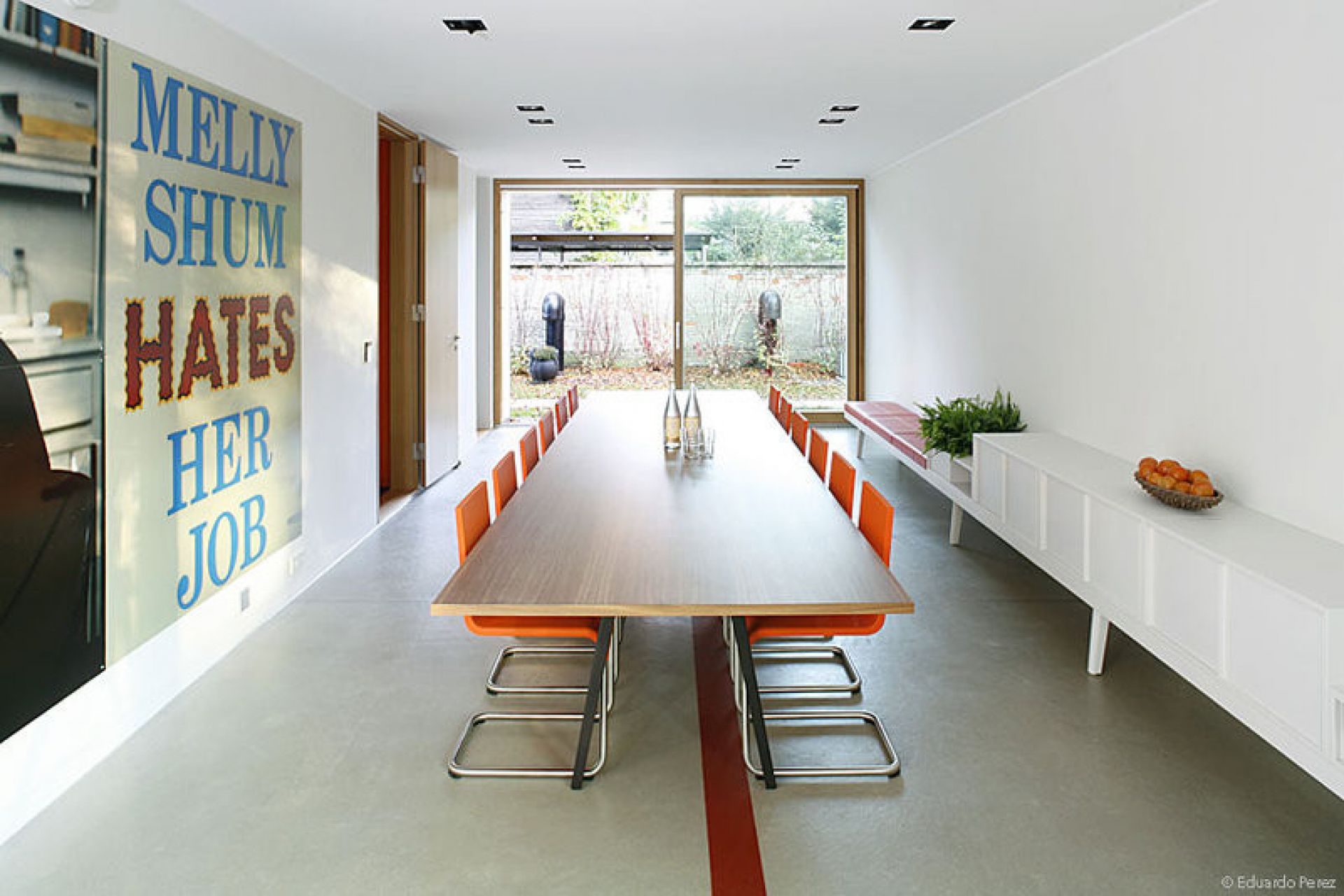 Langer Esstisch mit orangefarbenen .05 Stühlen von Vitra in einem modernen, hellen Esszimmer.
