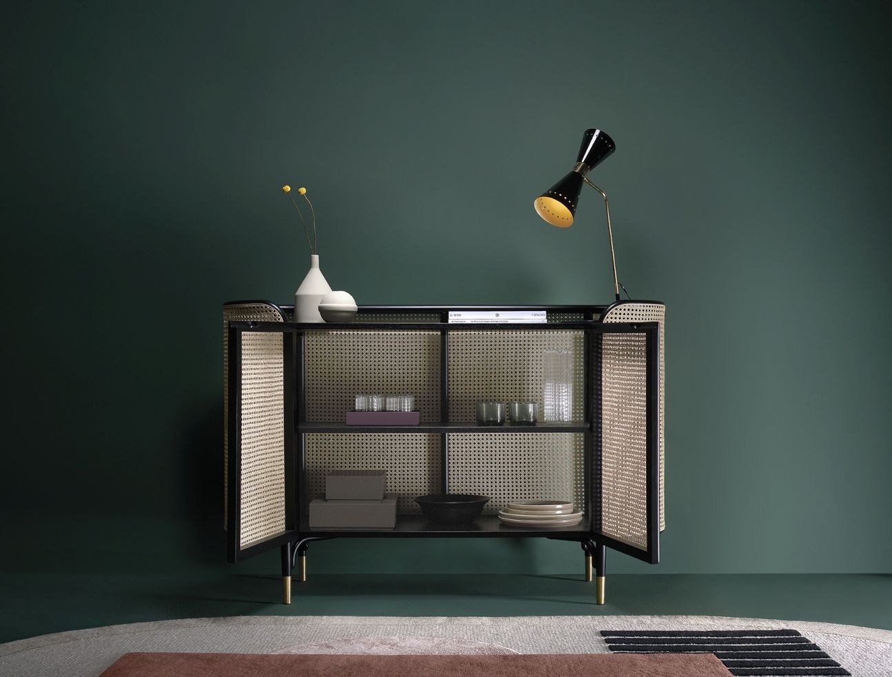 MOS CABINET Schrank von Wiener GTV Design mit offenen Türen und Rattan-Details vor dunkelgrünem Hintergrund.