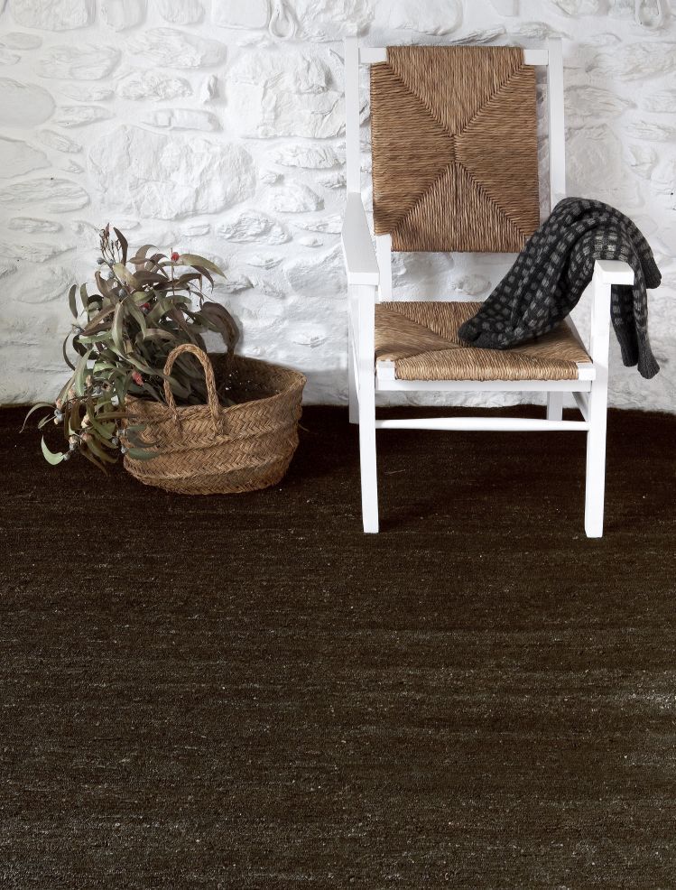 Nanimarquina Earth Rug Teppich in dunkler Farbe mit Stuhl und Korb im Raum.