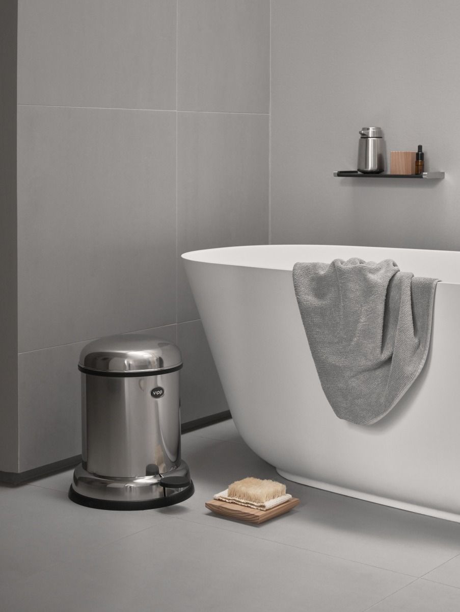 Vipp Treteimer aus Edelstahl im Badezimmer neben Badewanne und Seifenspender. Modernes Bad-Accessoire.