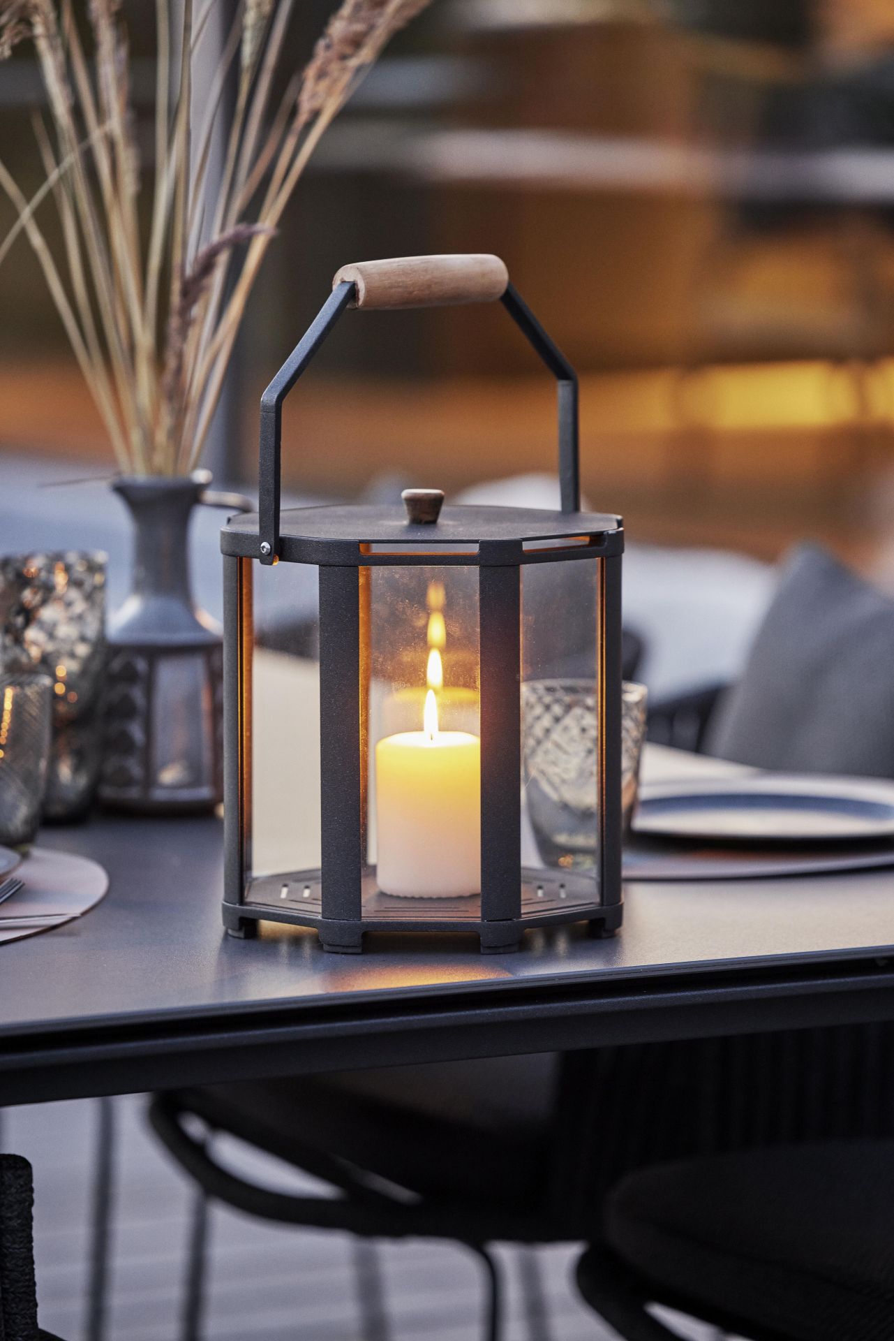 Lightlux Laterne Teak Large Cane-Line aus Teakholz und Metall mit brennender Kerze auf einem Tisch.
