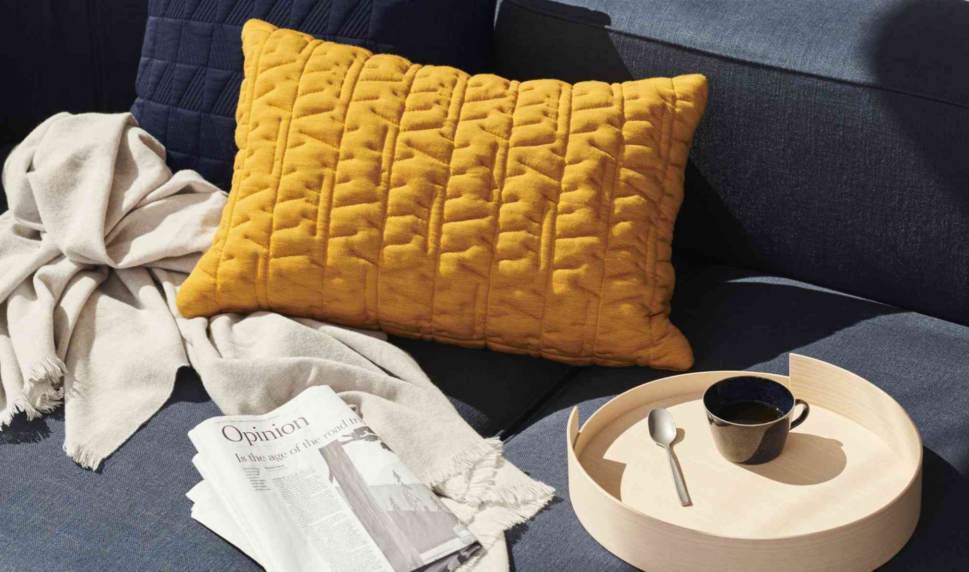 Detailaufnahme des Fritz Hansen Alphabet Sofas mit gelbem Kissen, Decke, Zeitung und Getränk auf einem Tablett.