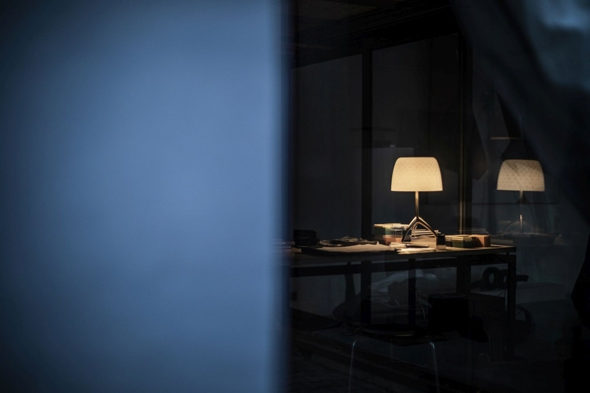 Lumiere Tischleuchte auf Schreibtisch mit Papieren und Büromaterialien, stimmungsvolle Beleuchtung im dunklen Raum.