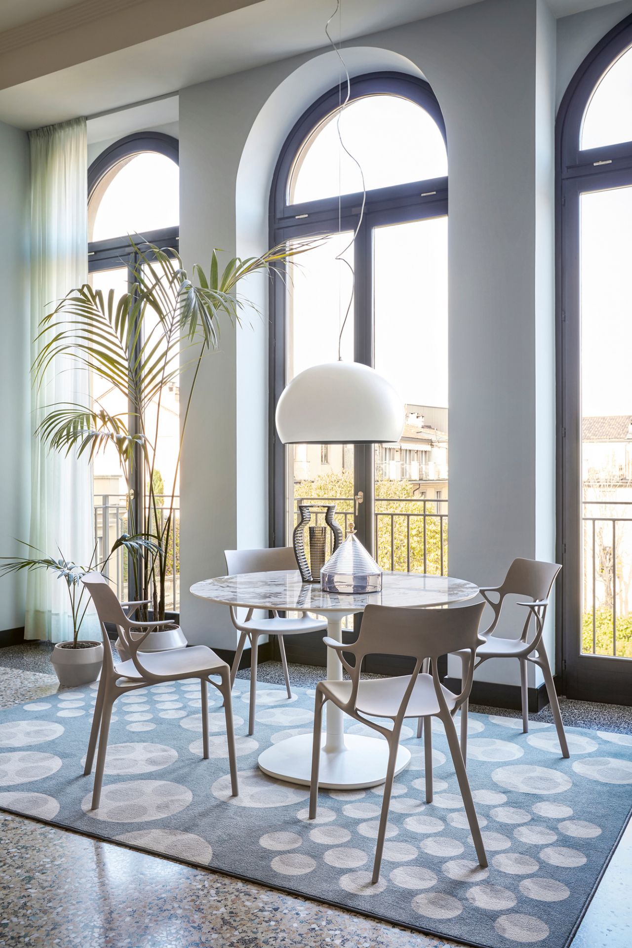 Esszimmer mit A.I. Stühlen von Kartell, modernem Design, hellen Fenstern und stilvollem Teppich.
