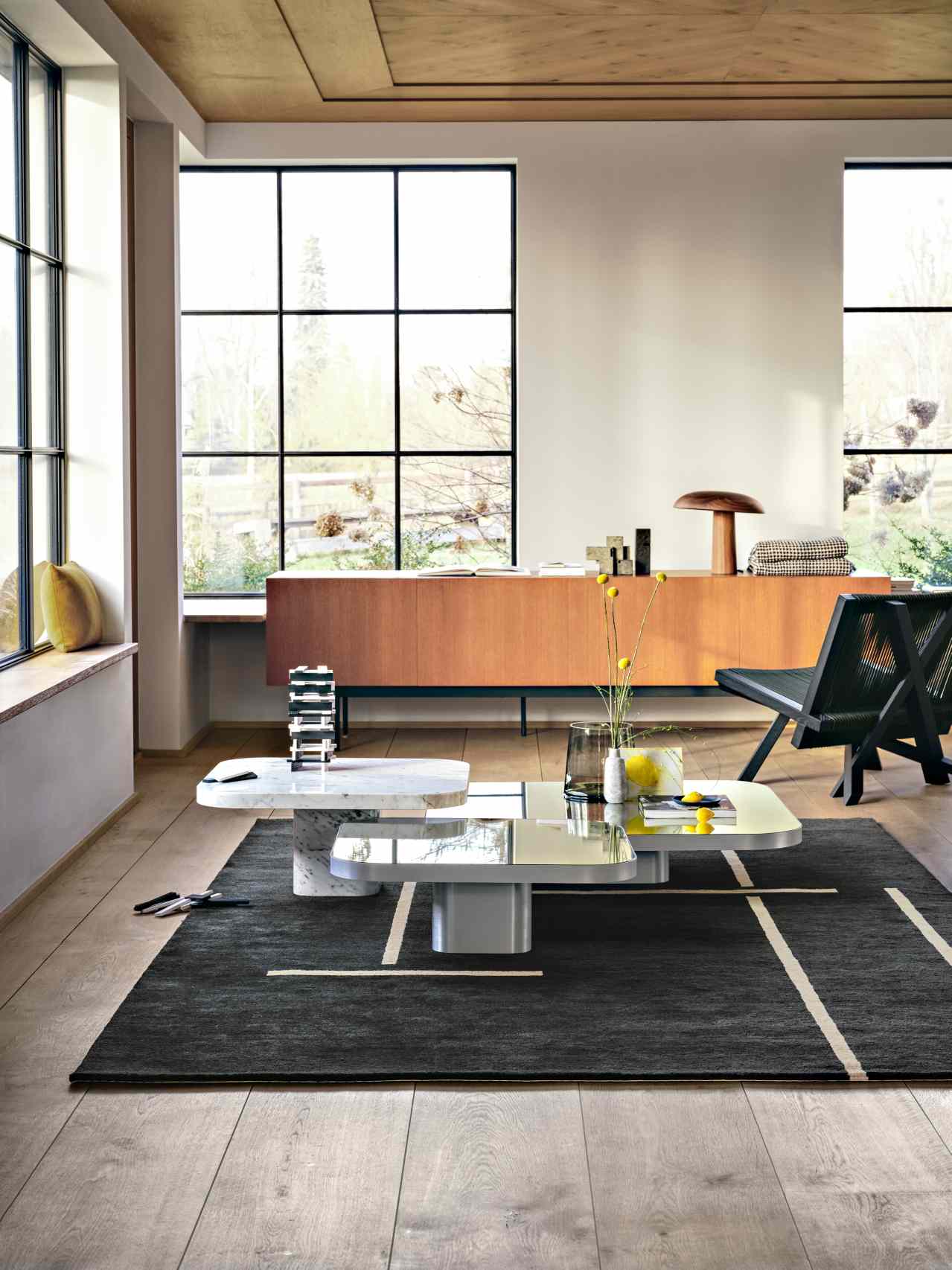 Moderner Wohnraum mit ClassiCon Bow Coffee Table, Marmor und Glas Couchtisch auf dunklem Teppich.
