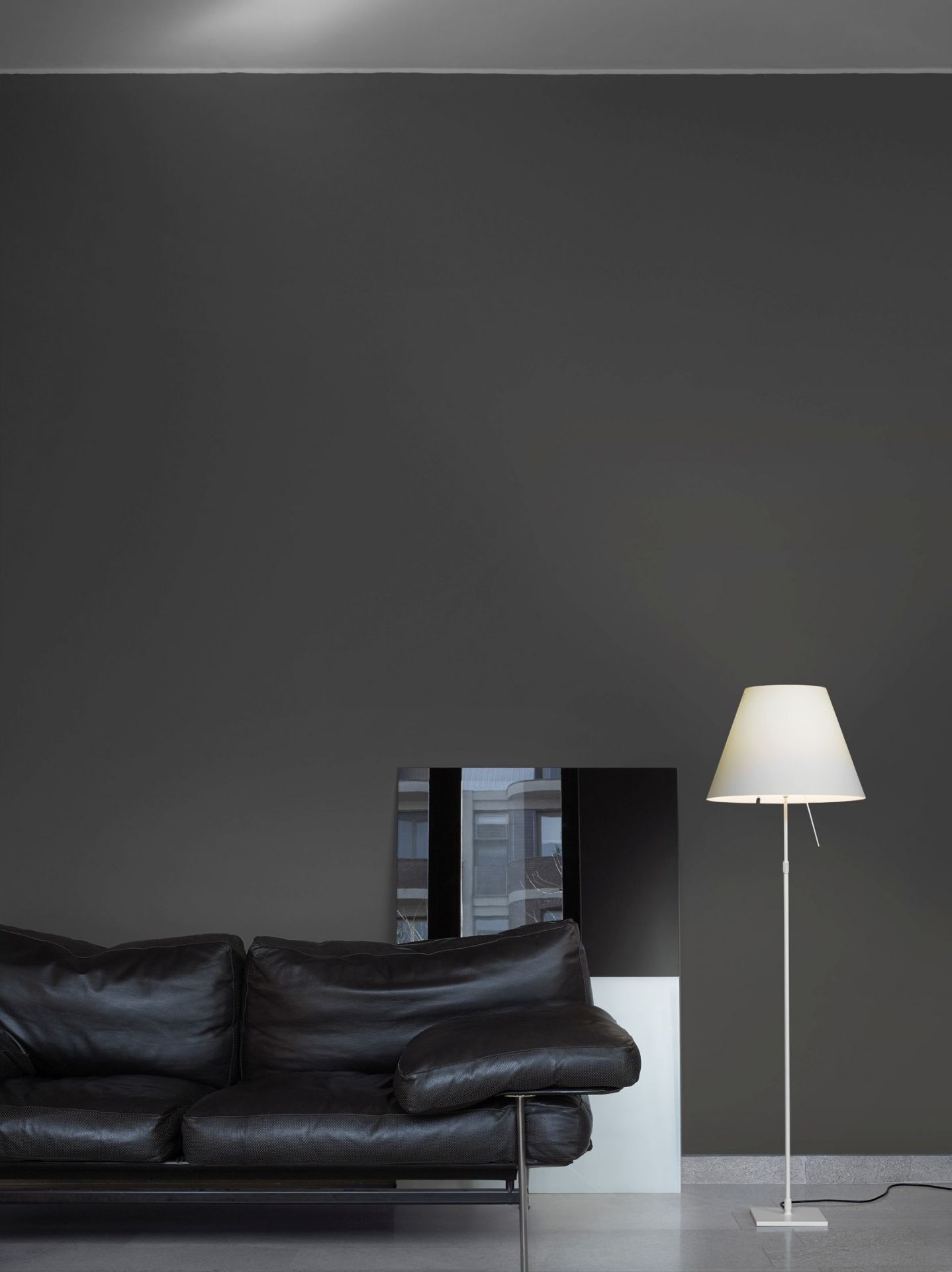 Helle D13 Costanza Stehleuchte von Luceplan neben dunklem Ledersofa in modernem Wohnzimmer.