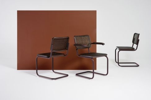 Drei braune Thonet S 64 V Freischwinger Stühle mit Stahlrohr und Wiener Geflecht vor braunem Hintergrund.