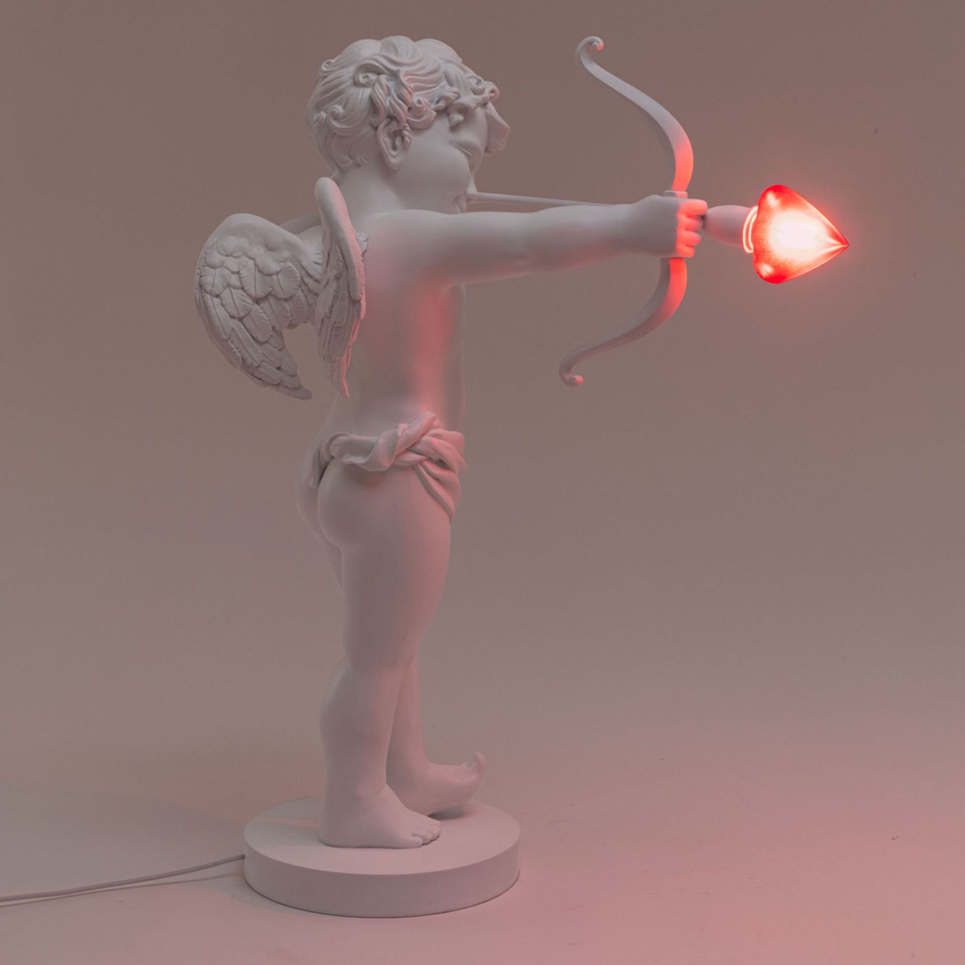 Weiße Cupid Lampe von Seletti, Amor mit Pfeil und Bogen, Herz leuchtet rot.