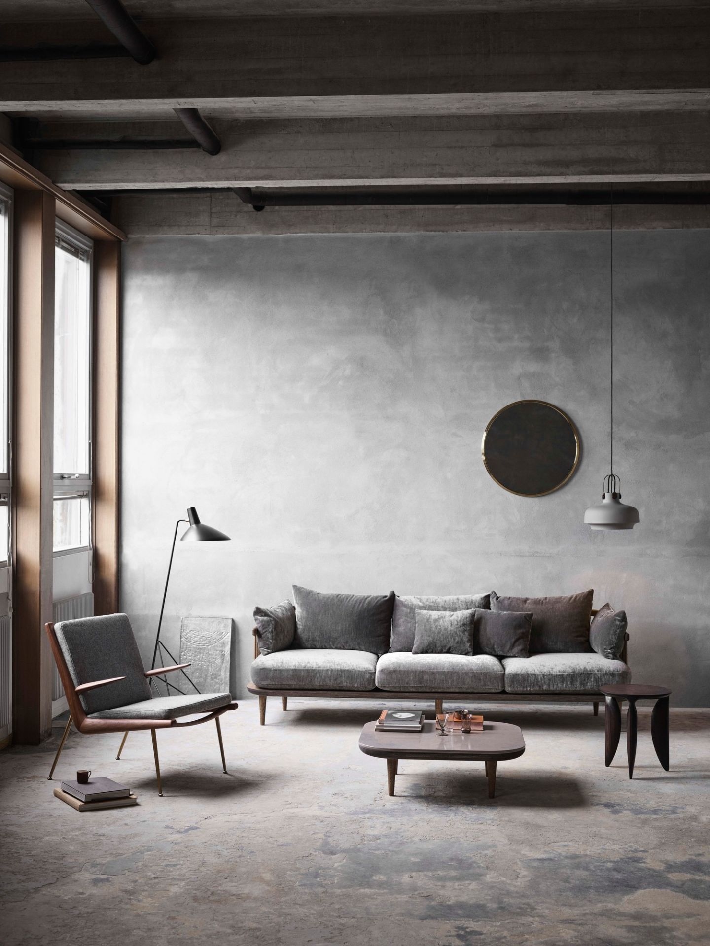 AndTradition Copenhagen SC7 Pendelleuchte über grauem Sofa in modernem Wohnzimmer mit Betonwand und Designermöbeln.