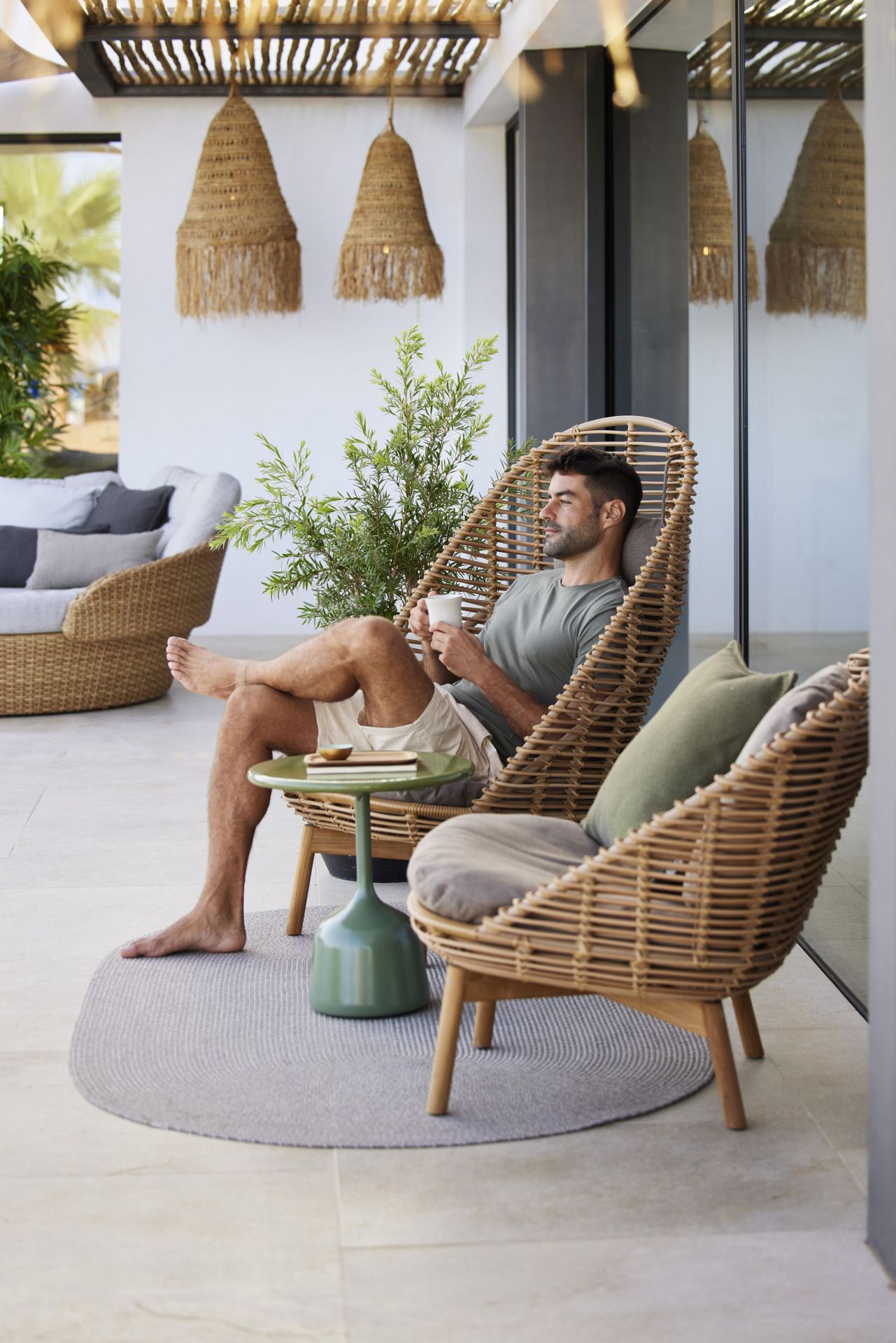 Mann entspannt im Cane-Line Hive Highbacksessel aus Teak mit Getränk auf der Terrasse.