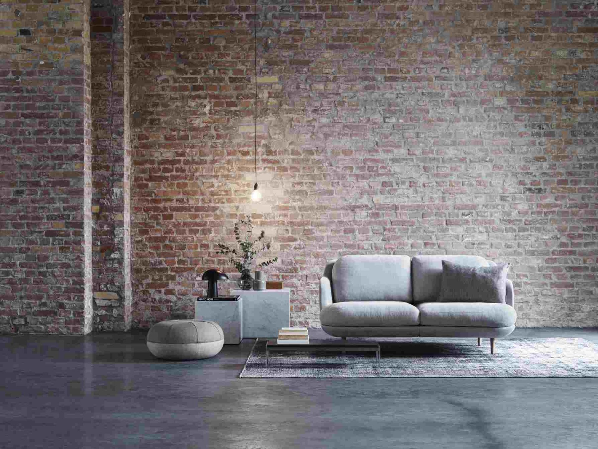 Graues Fritz Hansen Lune Sofa 2-Sitzer vor einer Backsteinwand, mit Beistelltisch und Teppich.