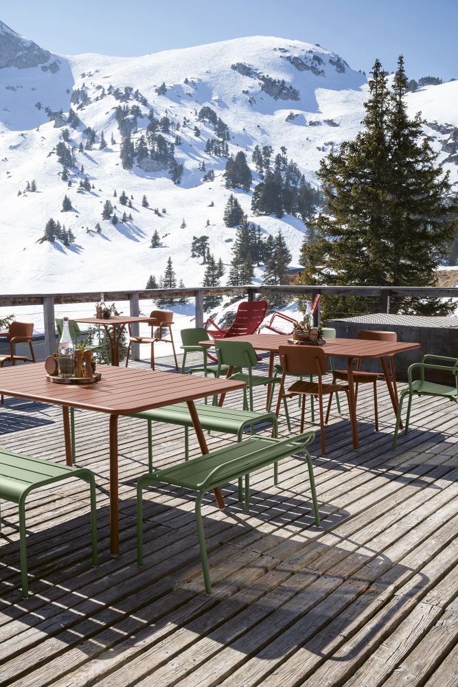 Fermob Luxembourg Outdoor Möbel: Tische, Stühle und Bank auf Holzterrasse mit Bergblick.