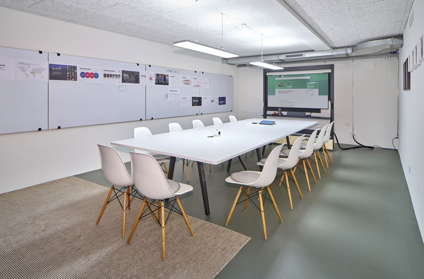 Konferenzraum mit langem Tisch und mehreren weißen Eames DSW Stühlen mit Sitzpolster von Vitra.