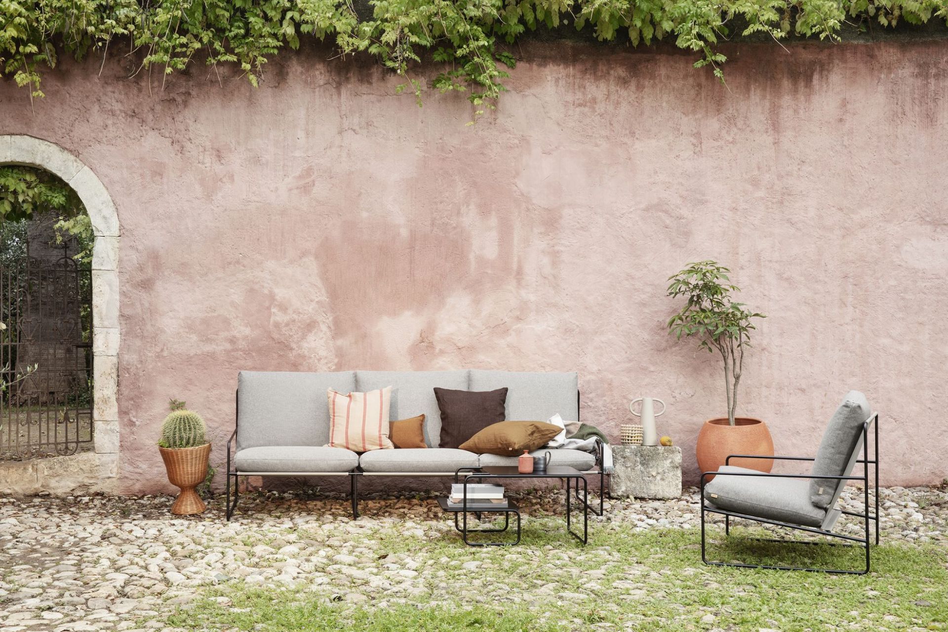 Desert 1-Sitzer Outdoor Sessel von Ferm Living mit schwarzem Gestell und grauer Polsterung im Garten.
